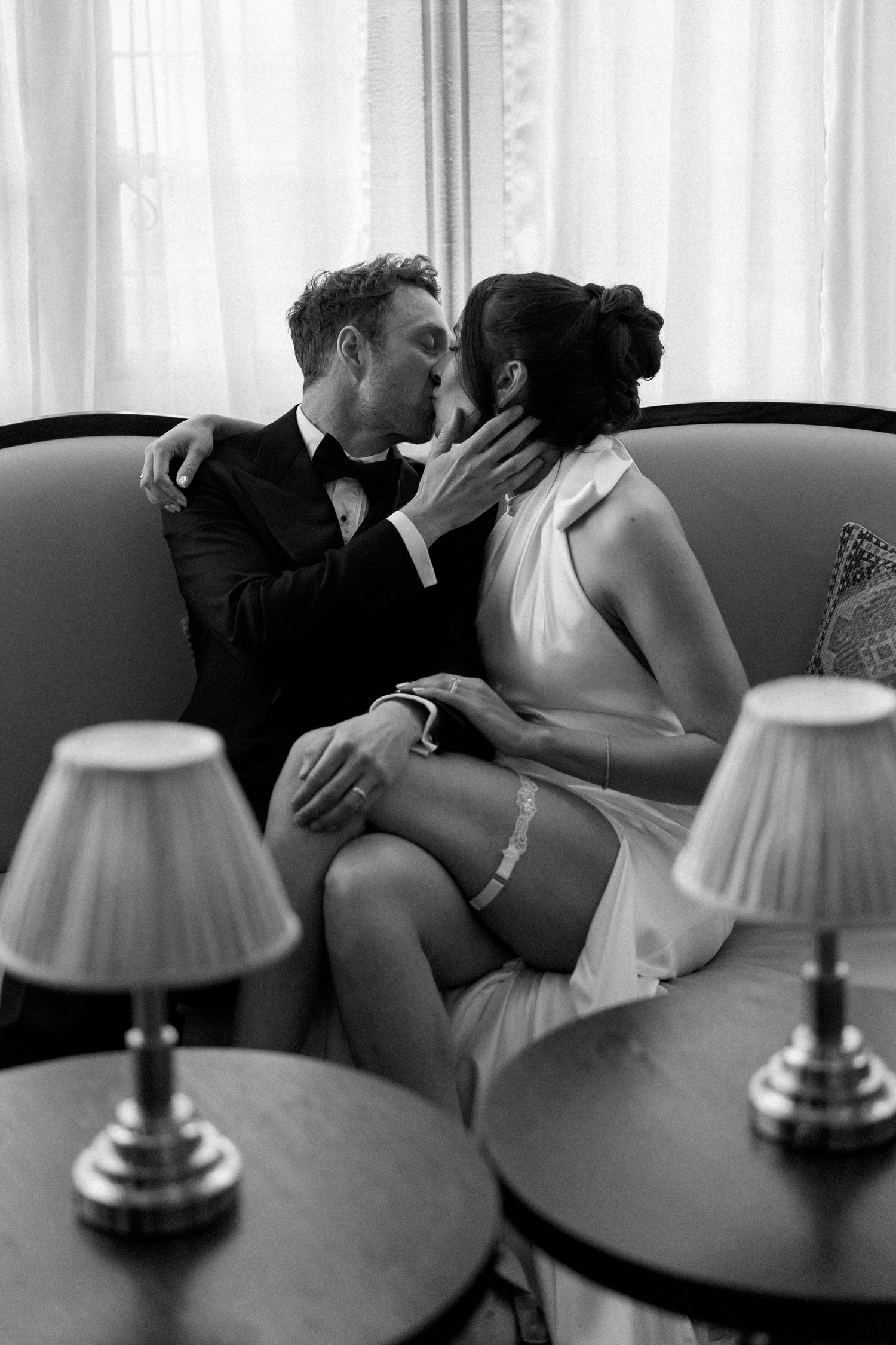 Black and white photo of bride and groom sharing intimate kiss on sofa.