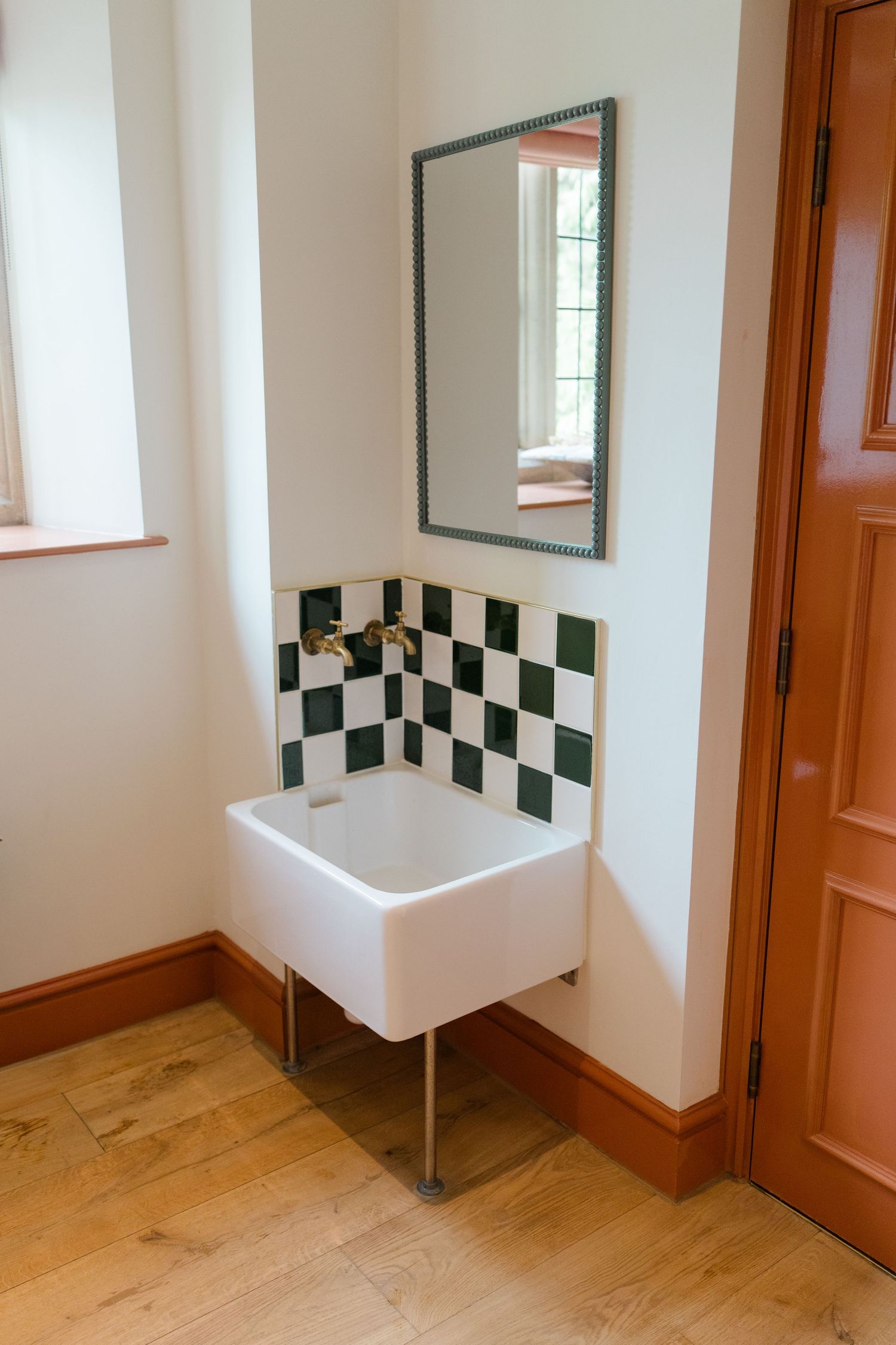 White ceramic sink with green checkered tiles and mirror in bright bathroom.