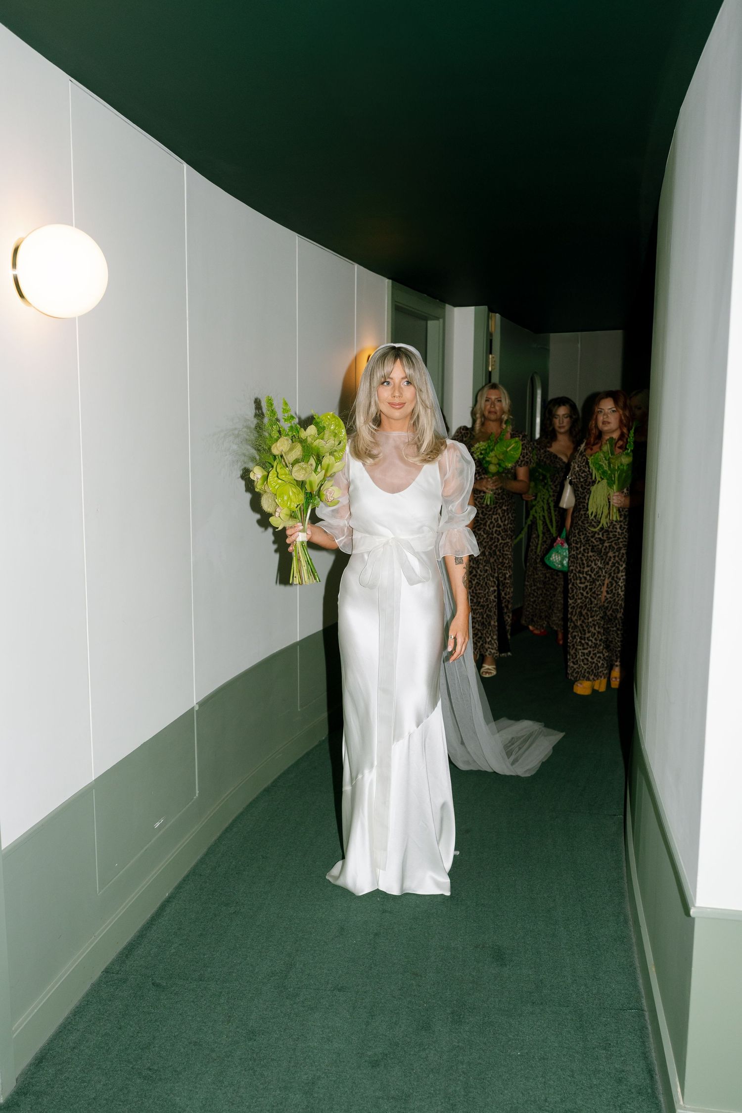 Elegant white silk wedding gown worn in a modern hallway with green walls.
