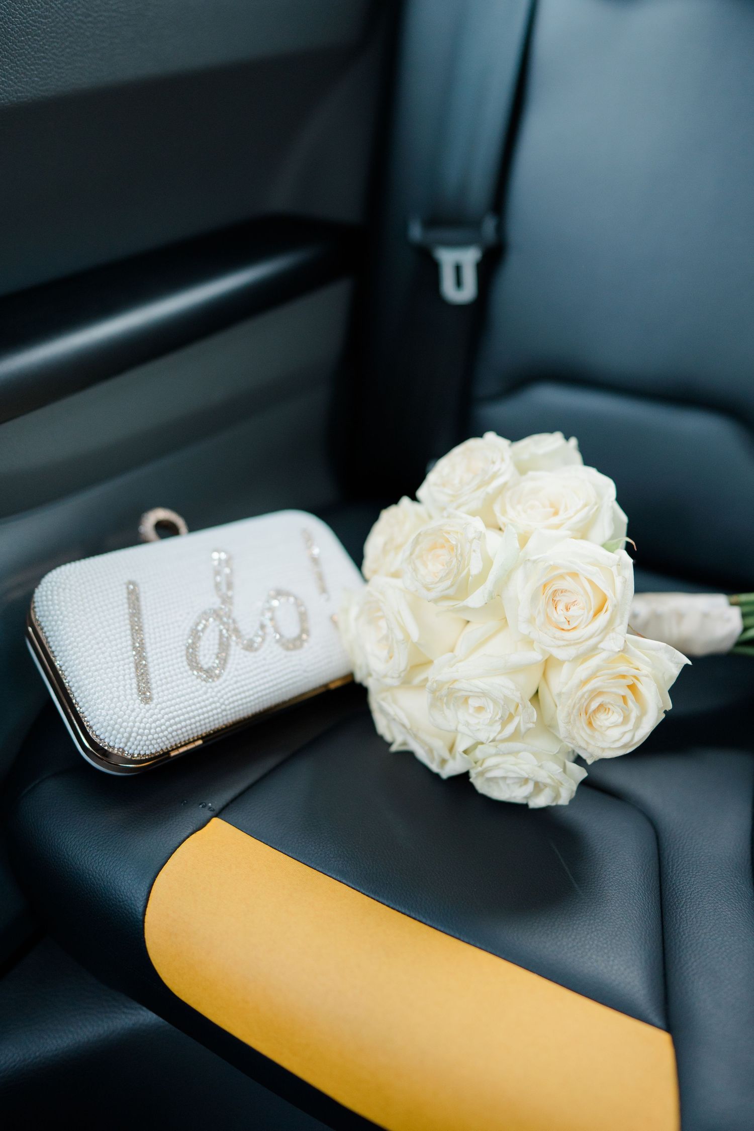 White roses and bridal shoes arranged on black leather car seat.