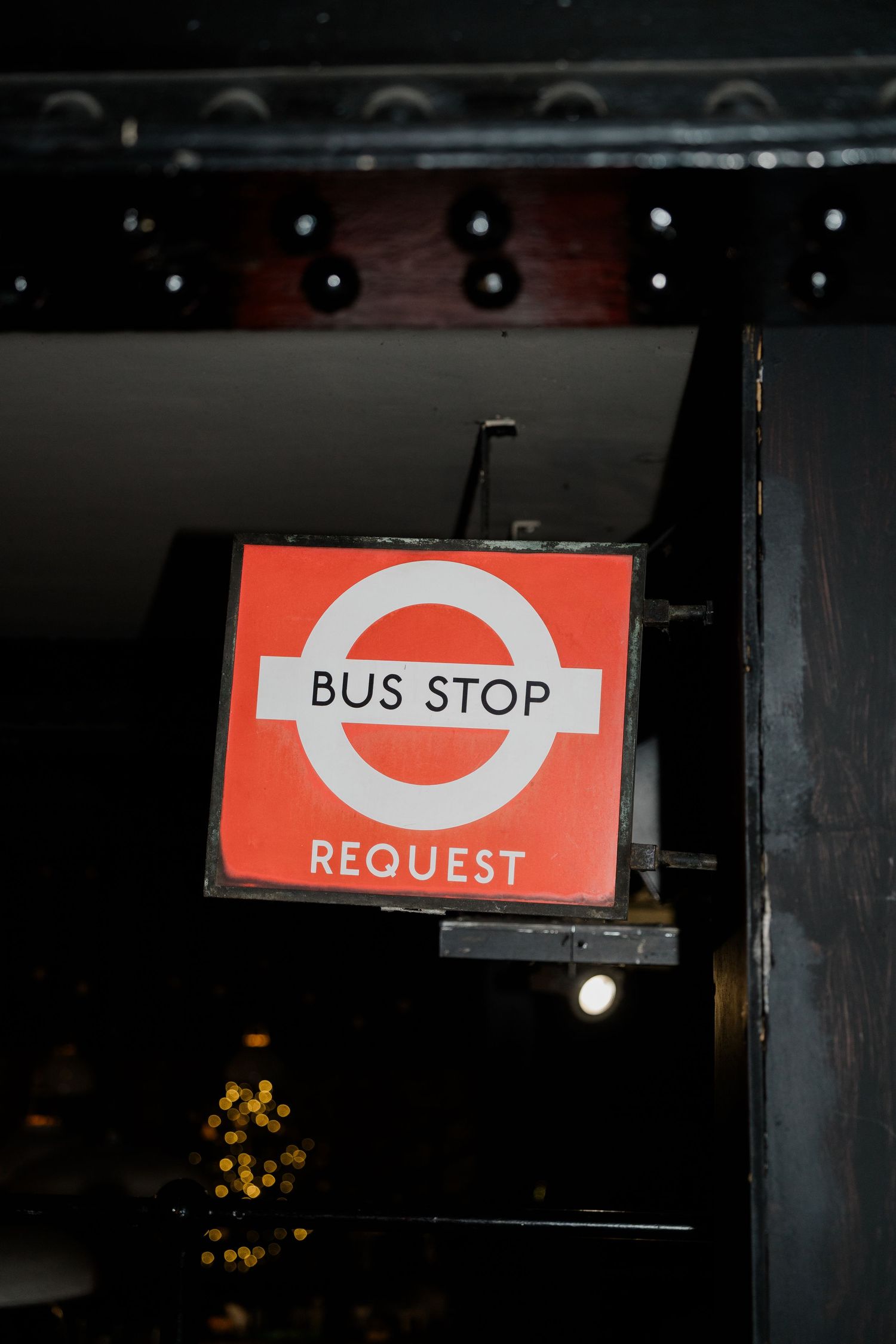 A red and white London bus stop request sign illuminated at night with bokeh lights in the background.