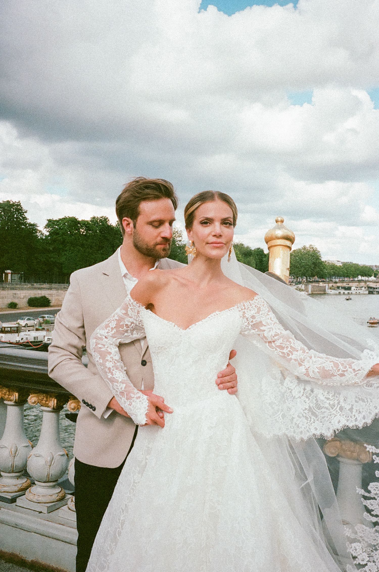 A romantic wedding couple poses together on a cloudy day near a marina with boats in the background.