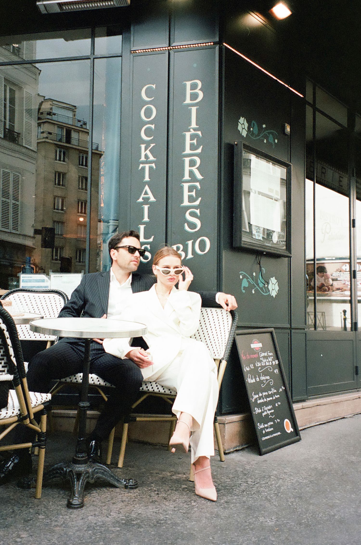 Two people relax on chairs outside a storefront with 'Bio' signage in an urban setting.
