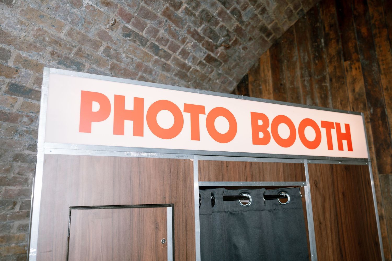 Photo booth sign mounted on brick wall at wedding venue.