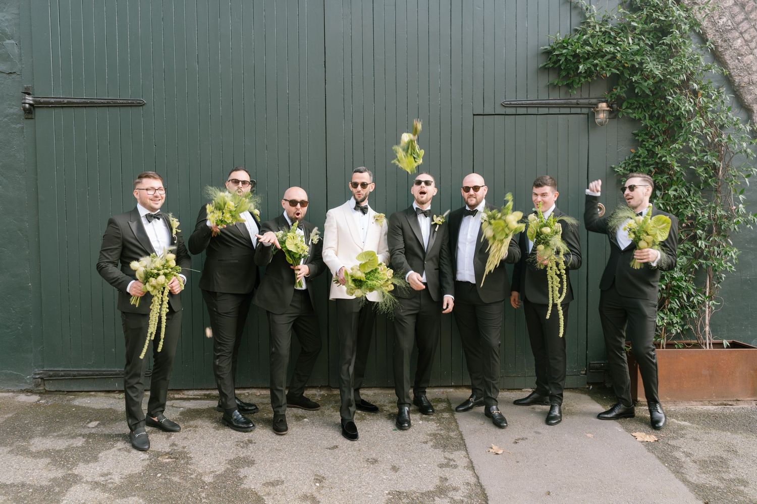 Wedding party members pose with yellow bouquets against industrial backdrop.