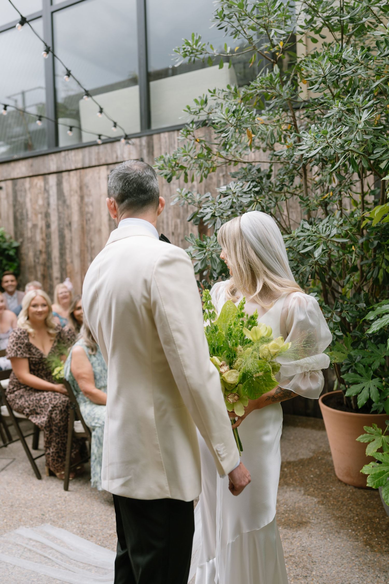 Wedding couple shares intimate moments in a greenhouse setting with greenery and string lights.