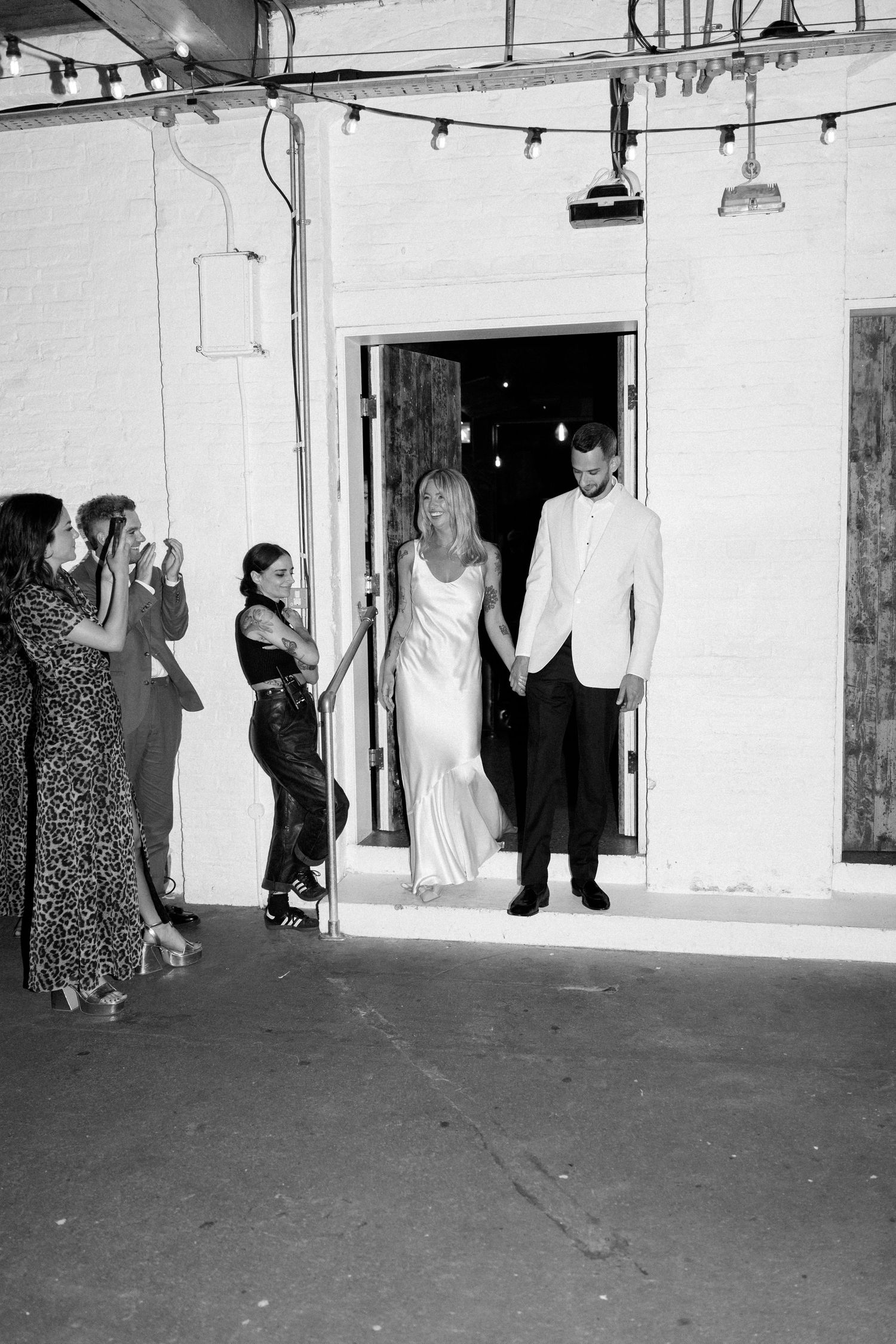 A black and white photo captures guests watching a couple make their entrance at a celebration.