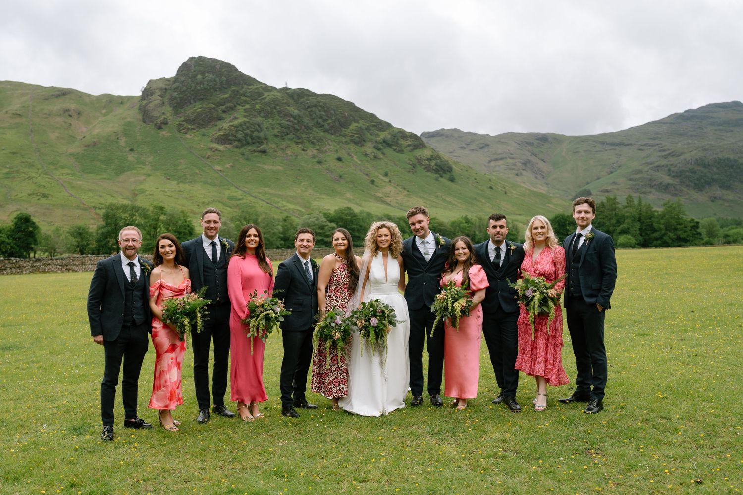 Wedding party in coral and black attire poses for group photos in a scenic mountain setting.