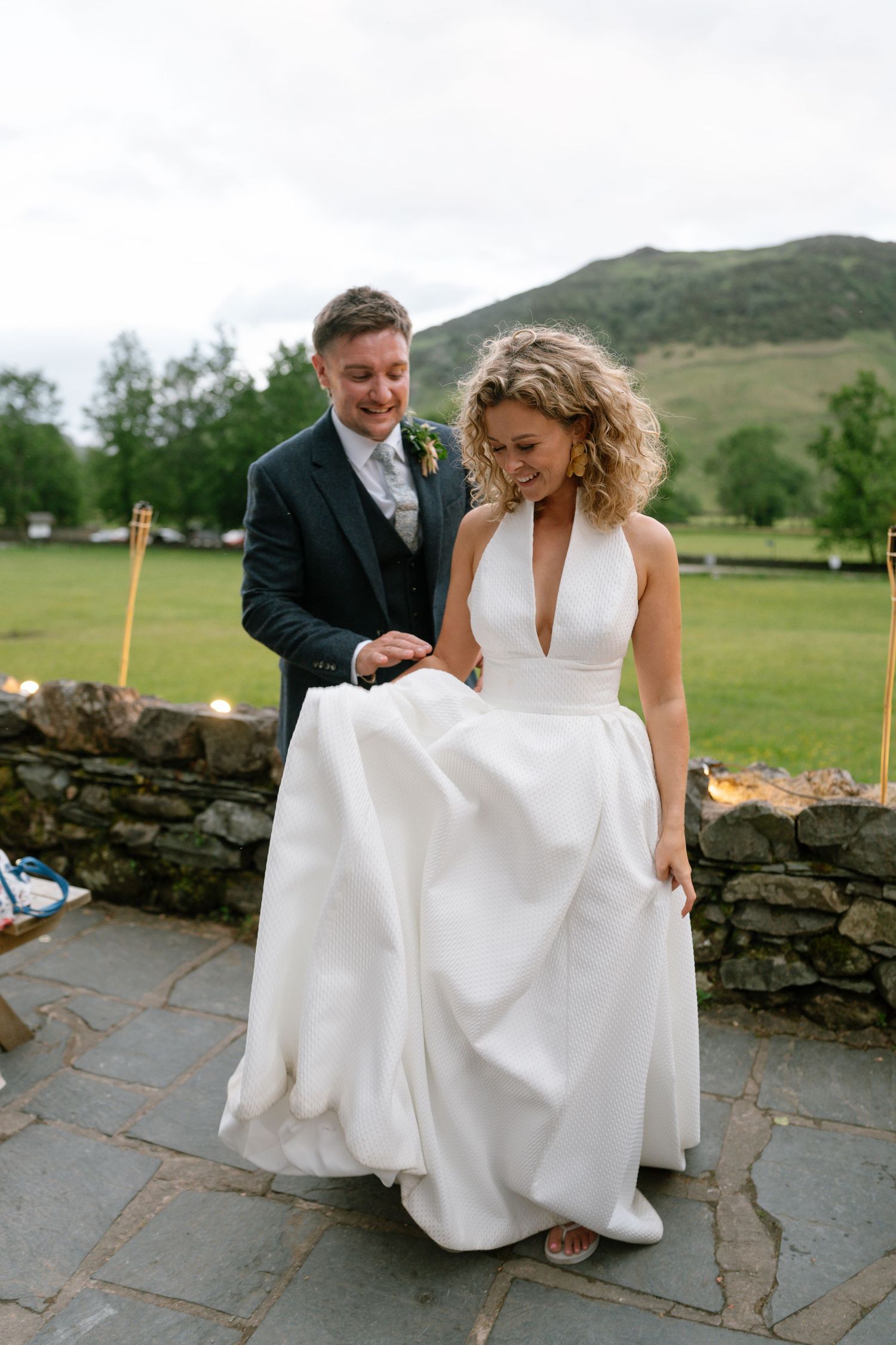 A couple walks along stone pathways surrounded by green hills during their wedding celebration.