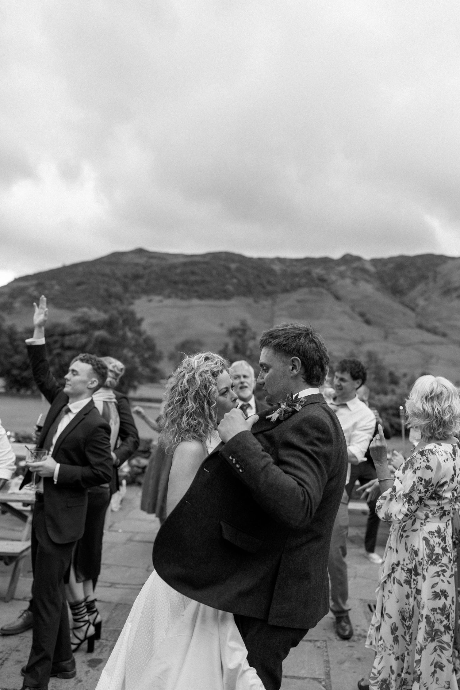 Wedding guests toast and celebrate outdoors with mountains and cloudy skies as the backdrop.