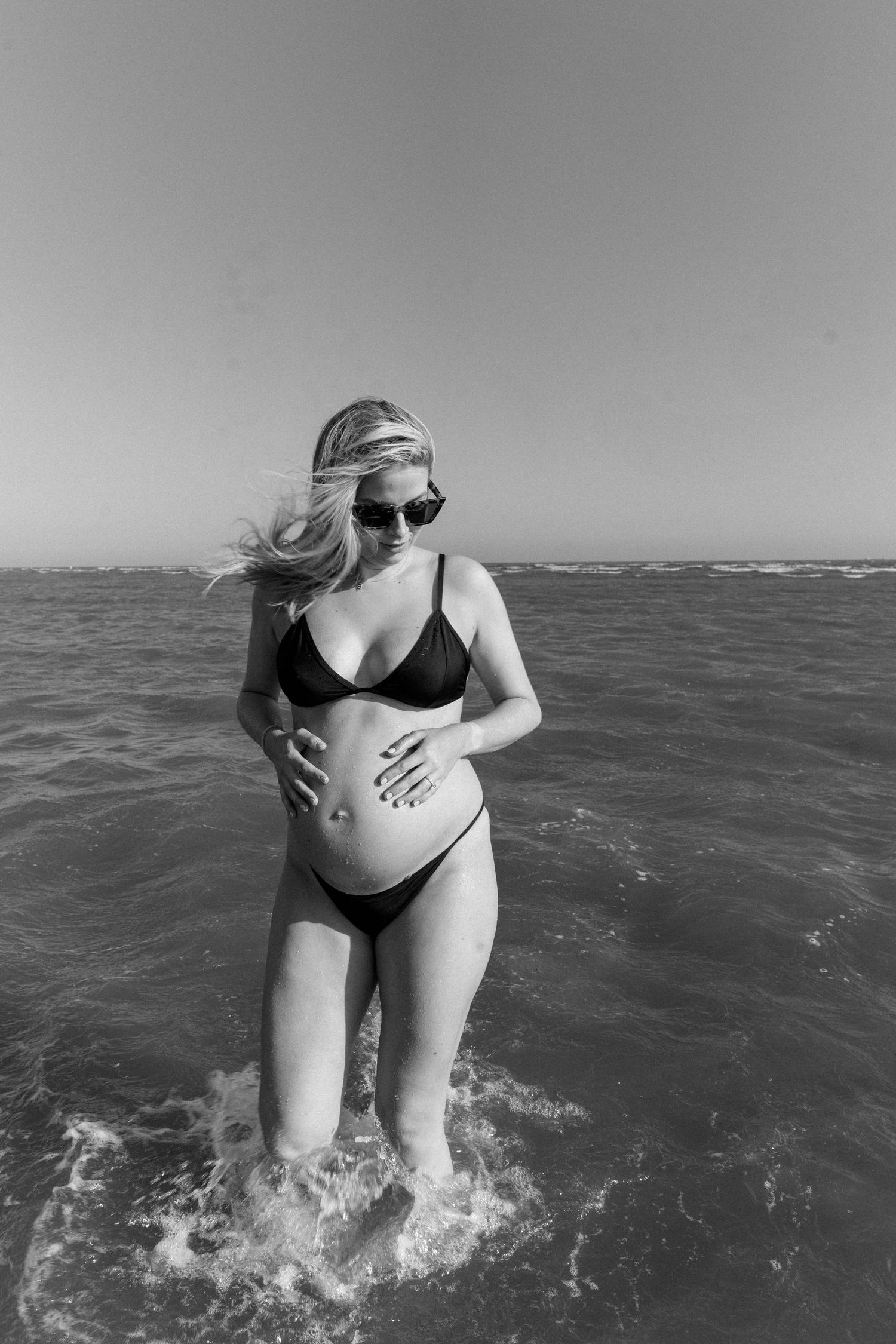 Black and white image of someone wading in ocean waves on a sunny day.