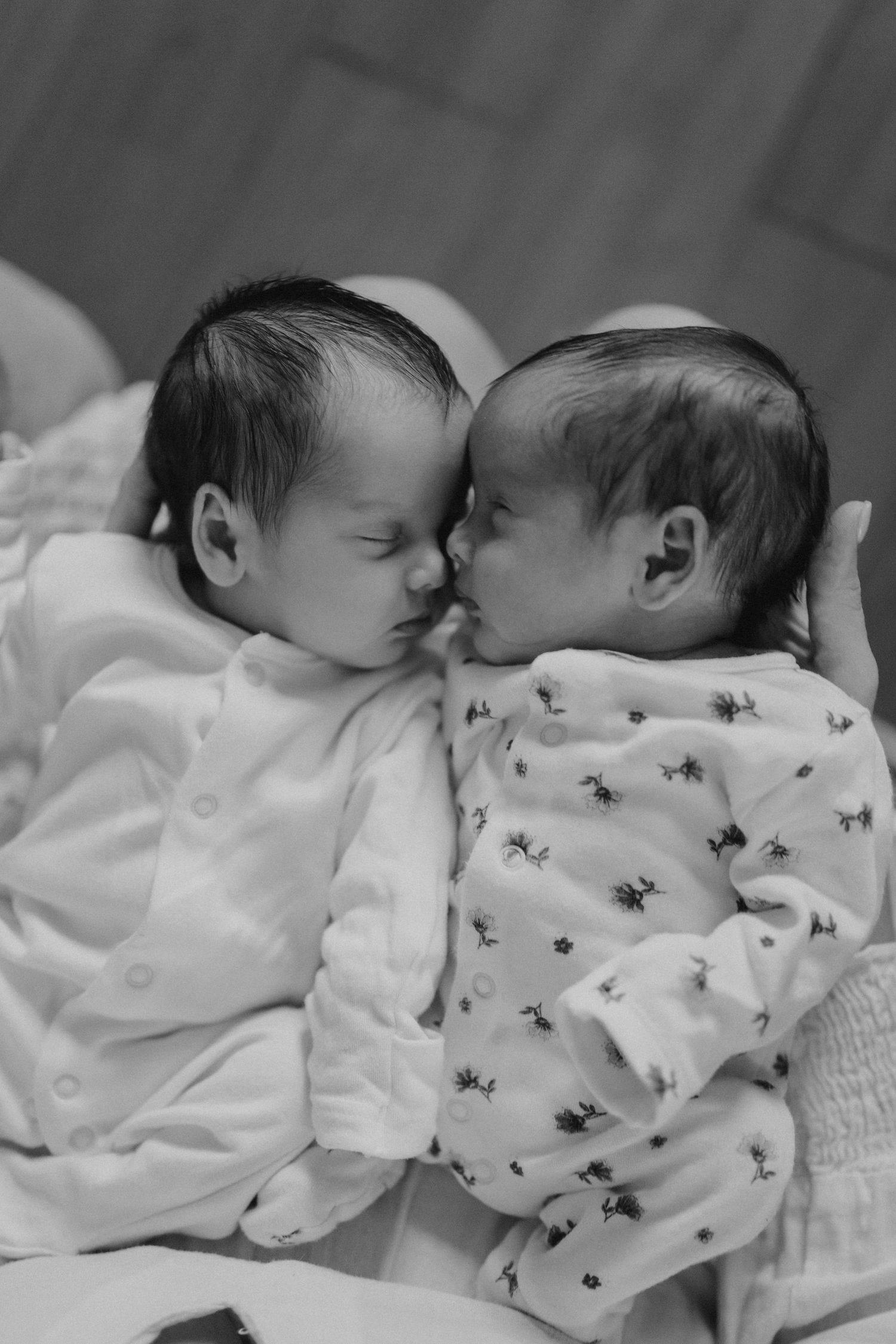 Two babies in patterned white sleepwear rest close together.