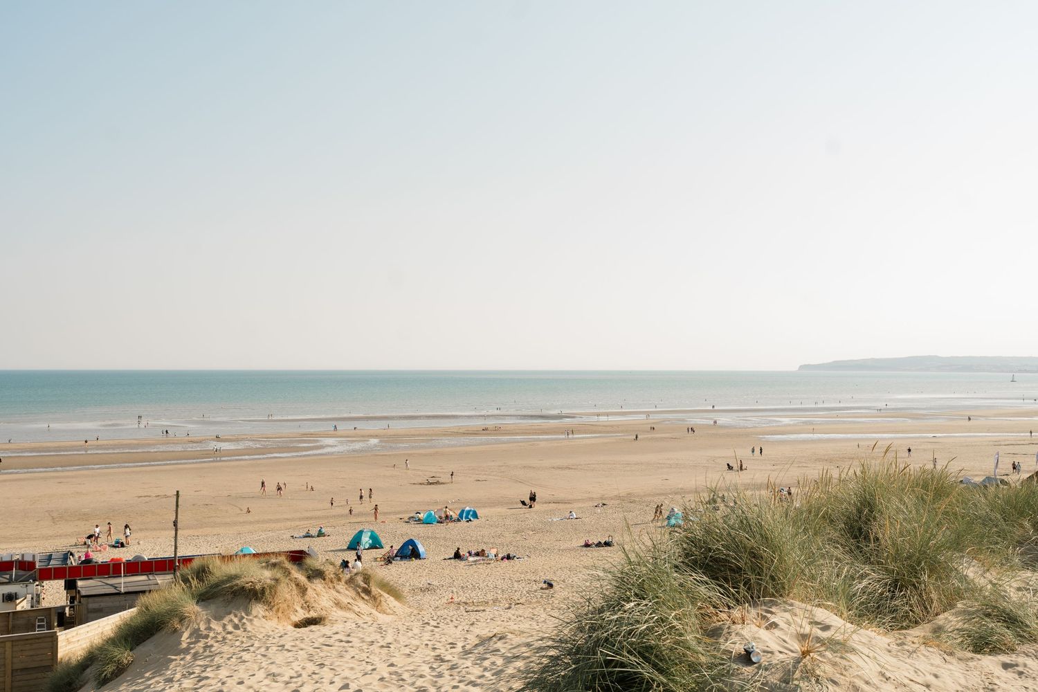 Wide view of a sandy beach with distant beachgoers and blue ocean on a clear day.