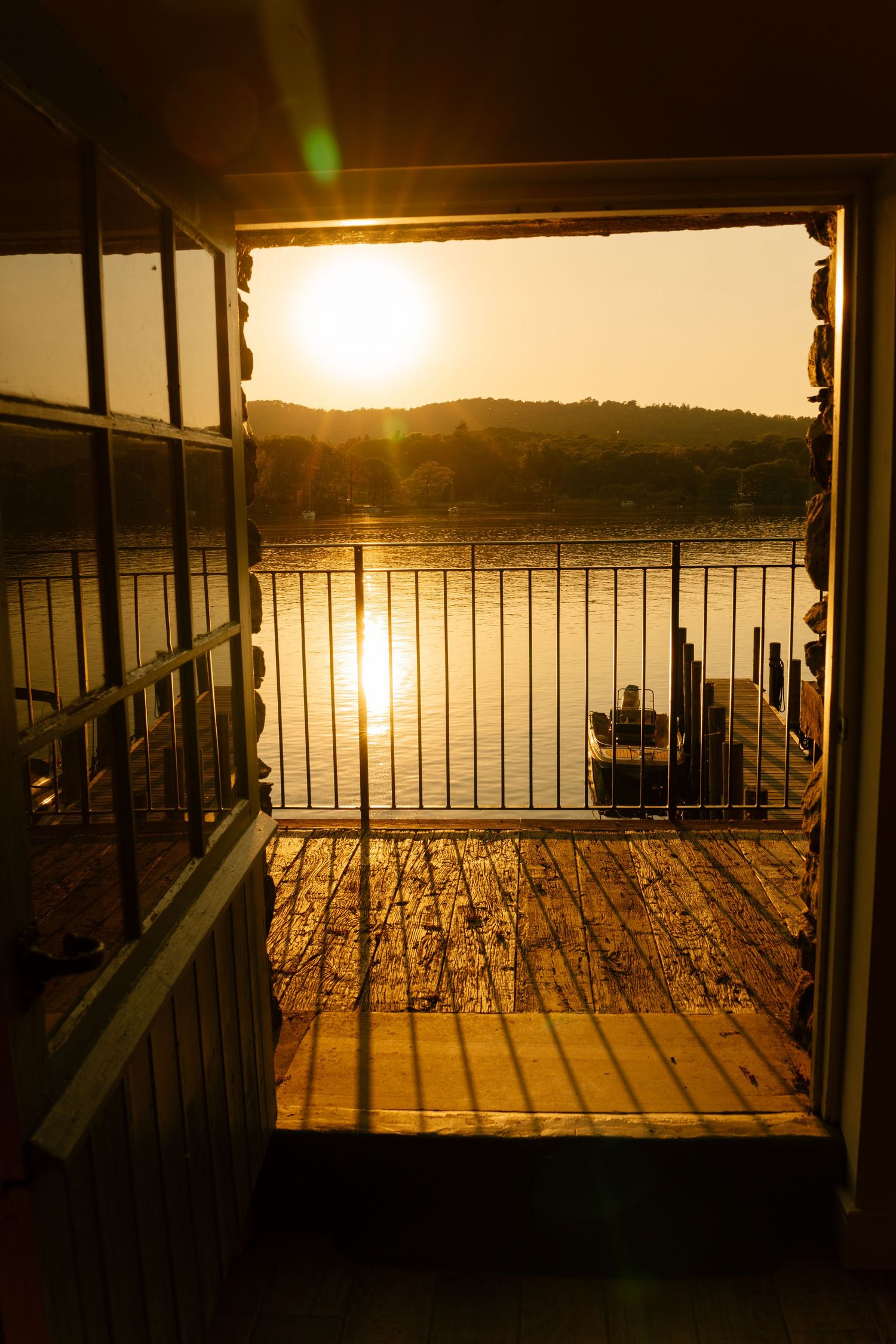 Golden sunset view over a lake through deck railings creating dramatic shadows.