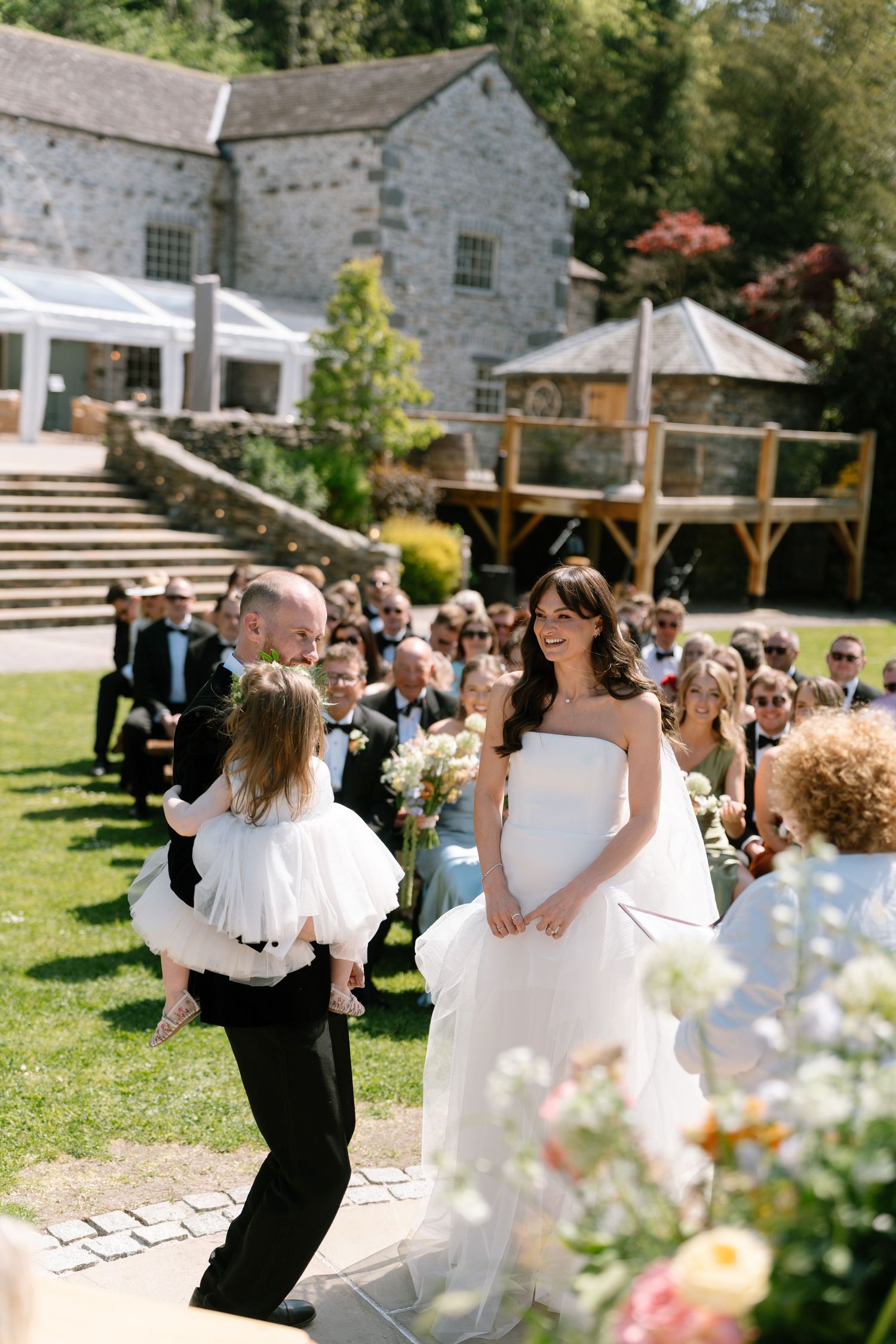Wedding celebration in garden setting with stone buildings and wooden pergola.