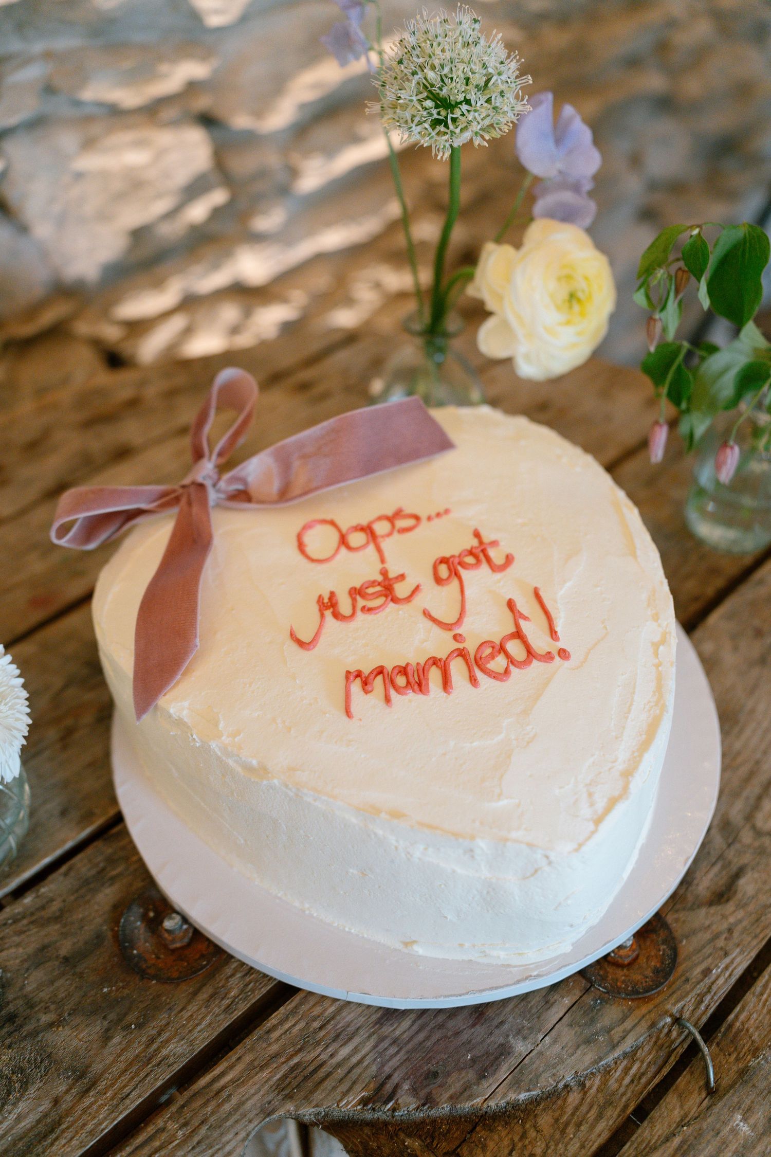 White wedding cake with pink bow and 'Oops... just got married!' text decoration.