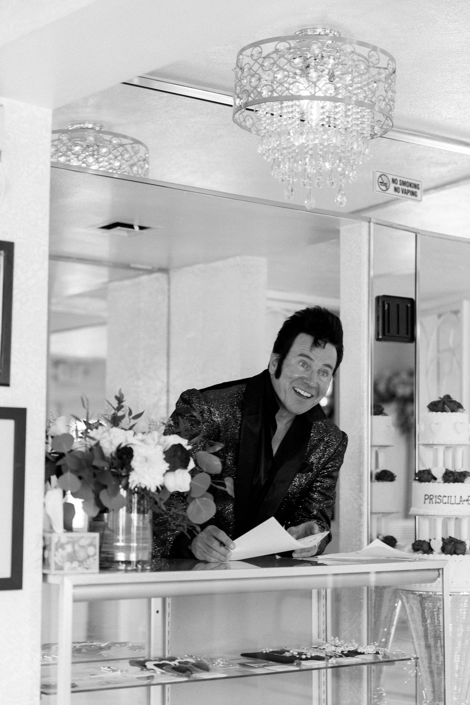 Wedding officiant reviews paperwork at chapel counter with crystal chandeliers overhead.