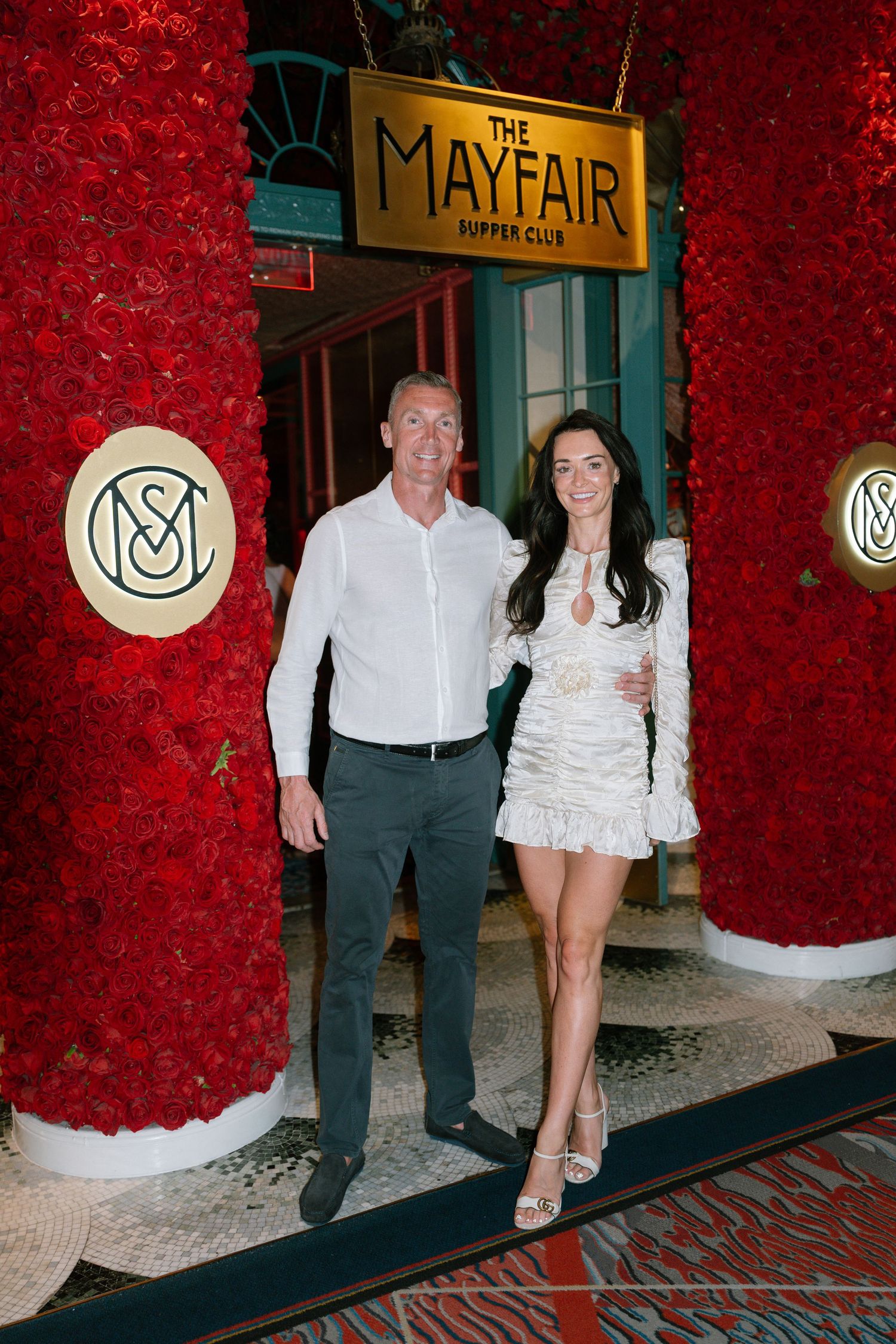 A couple stands in front of the Mayfair Supper Club entrance with red floral decor.