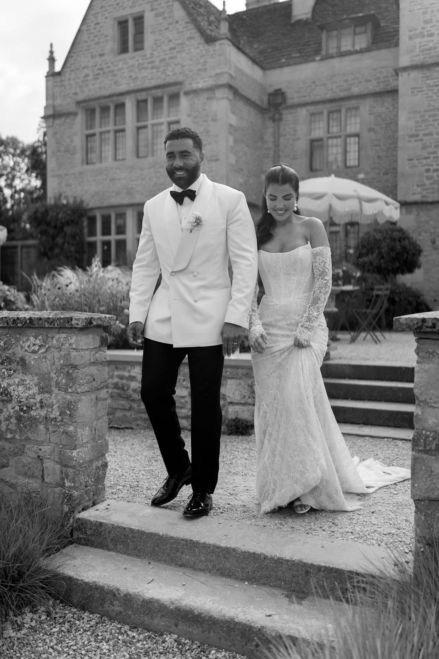 Black and white portrait of bride and groom posing on stone steps outside historic English manor house.