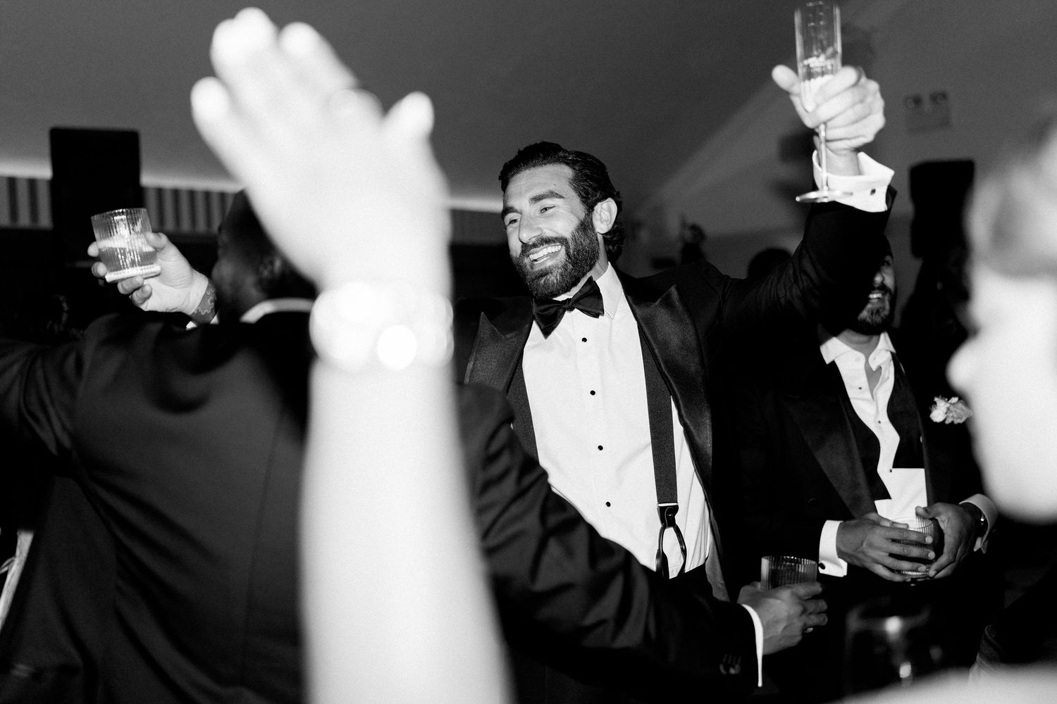 Smiling groom in tuxedo raises glass on the dance floor at wedding reception.