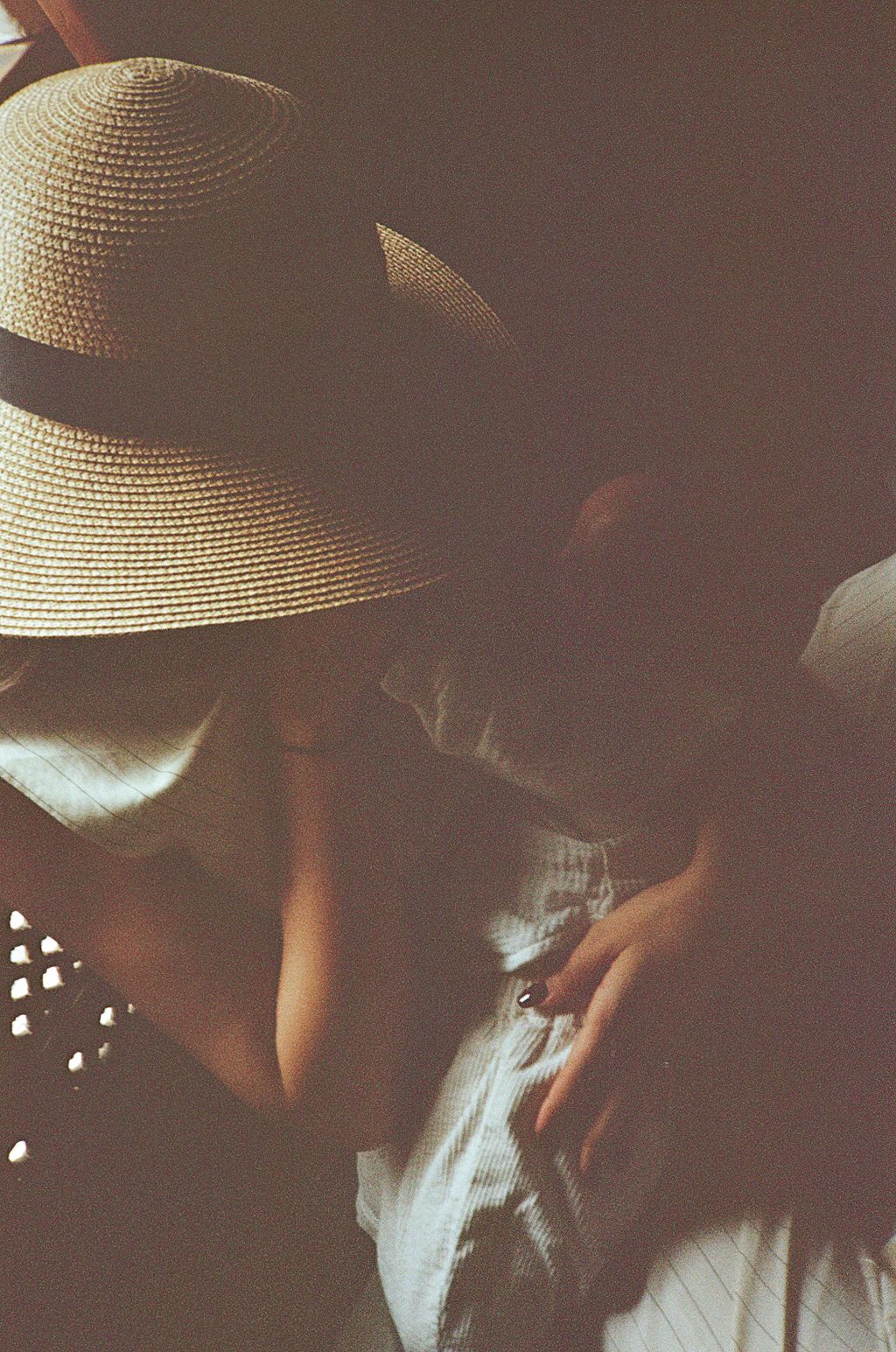 A woman wearing a wide-brim straw sun hat with a dark band, shot in moody, vintage film photography style.