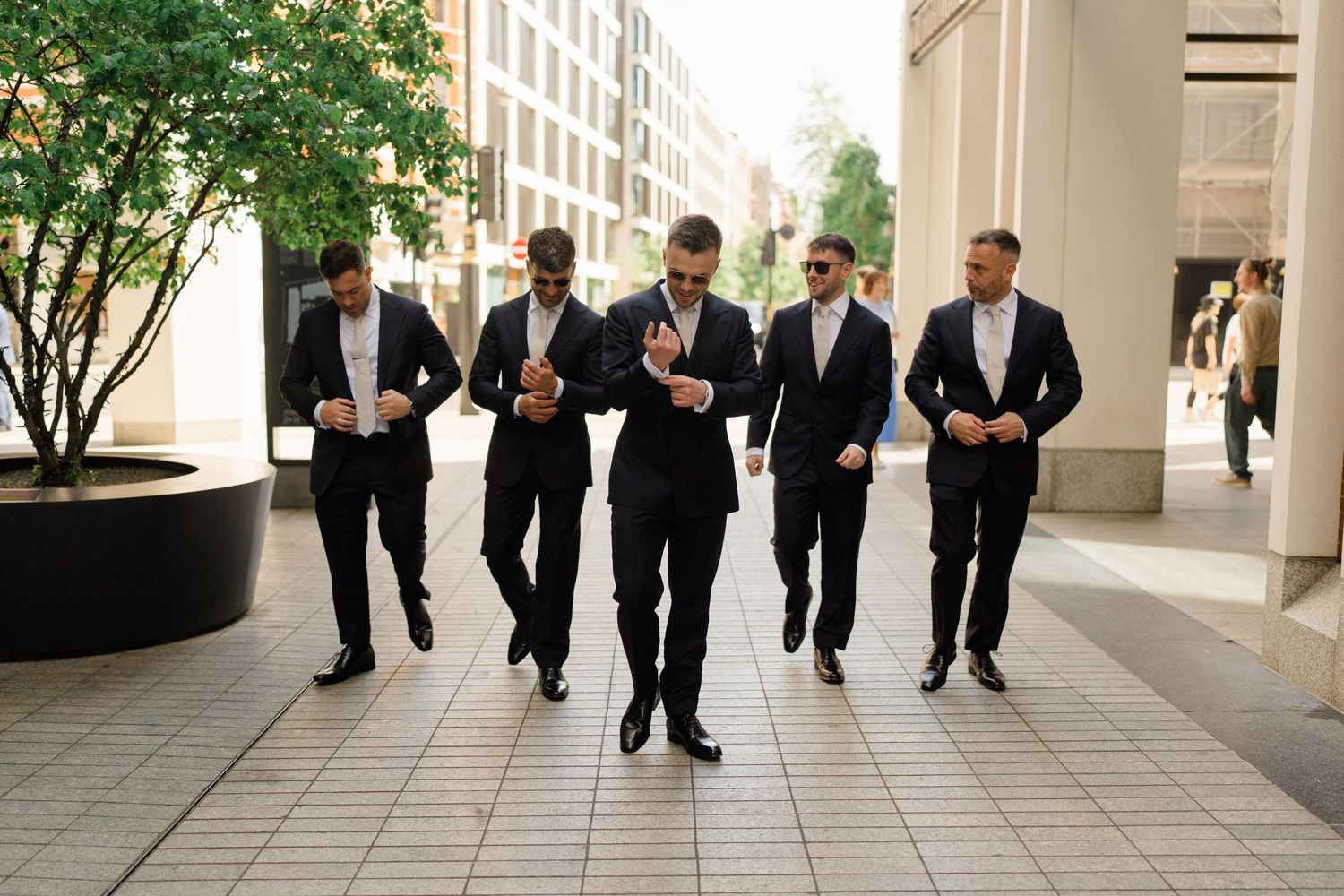 Groom and groomsmen in black suits walking confidently together on city street.