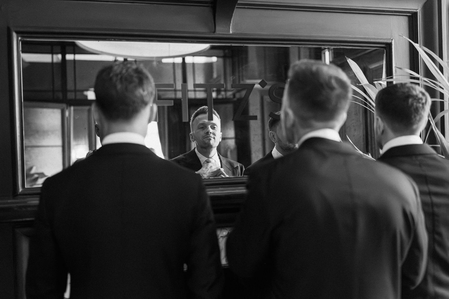 Two men in suits stand before a mirror in a black and white photo, reflecting a formal occasion.
