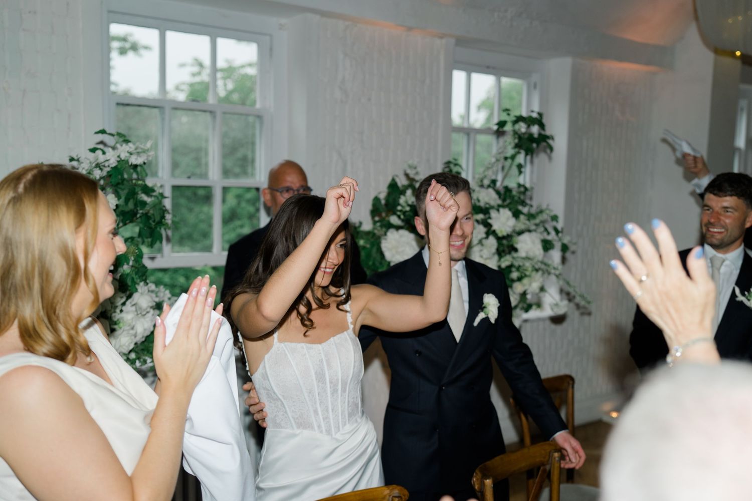 Bride and groom laugh and clap together as guests celebrate their entrance at wedding reception.