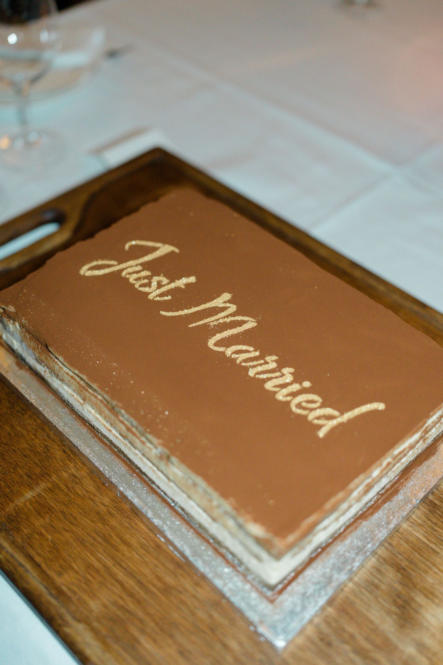 Rectangular chocolate wedding cake inscribed with Just Married in gold lettering on wooden serving board.