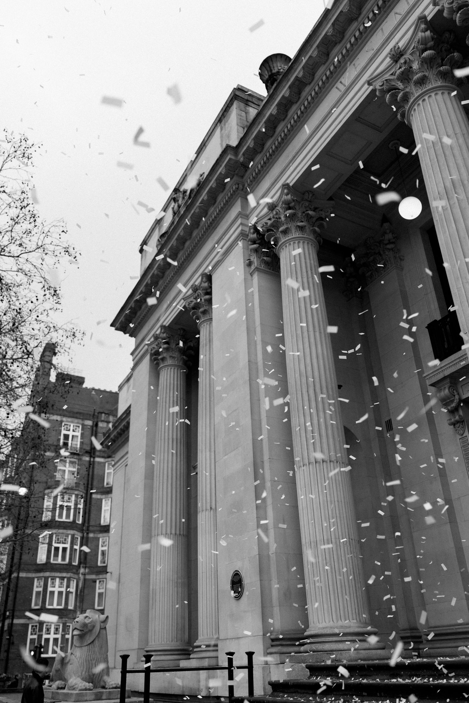 Black and white photo of confetti falling outside neoclassical wedding venue with tall stone columns.