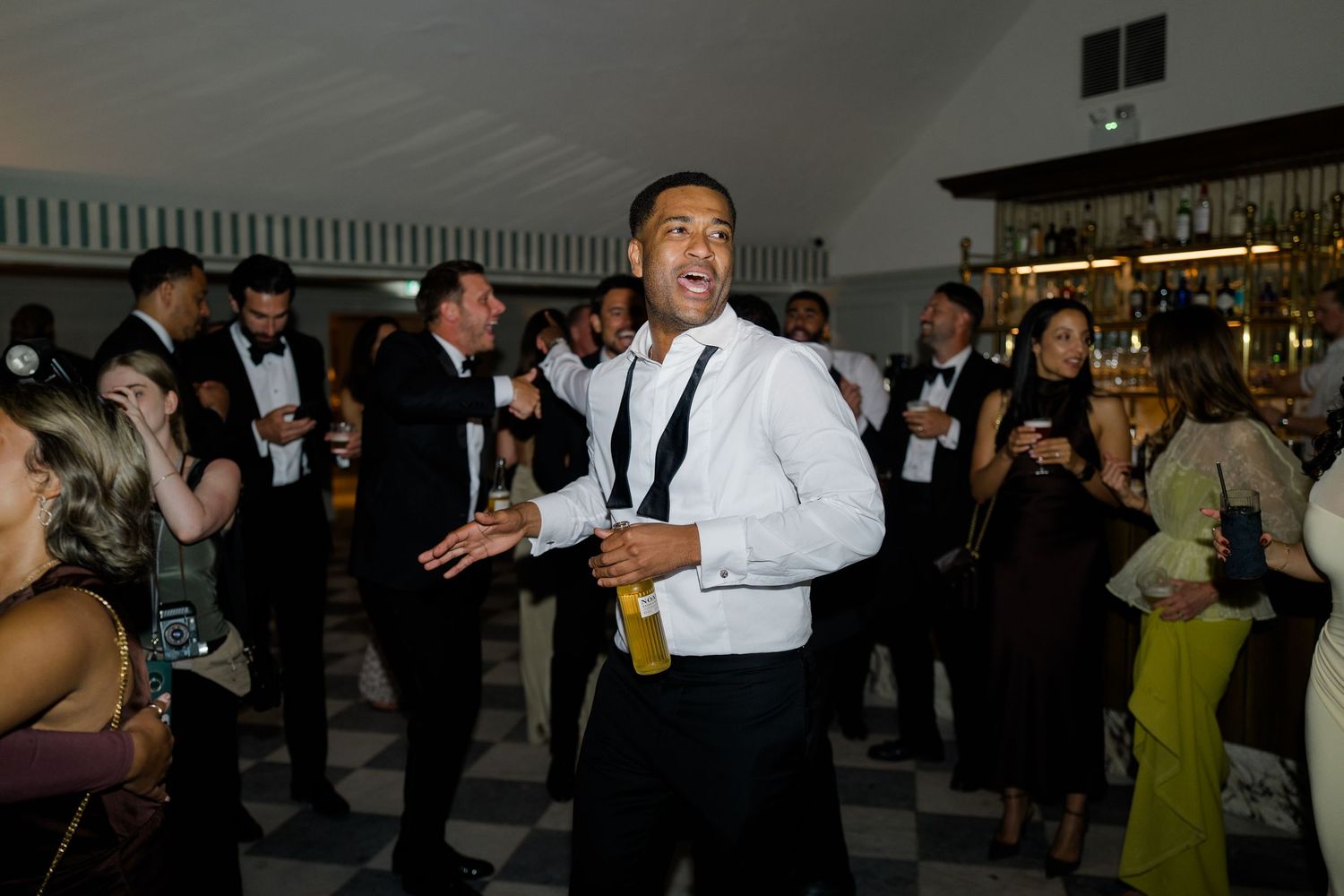 Male wedding guest dancing enthusiastically with suspenders at elegant black and white reception.