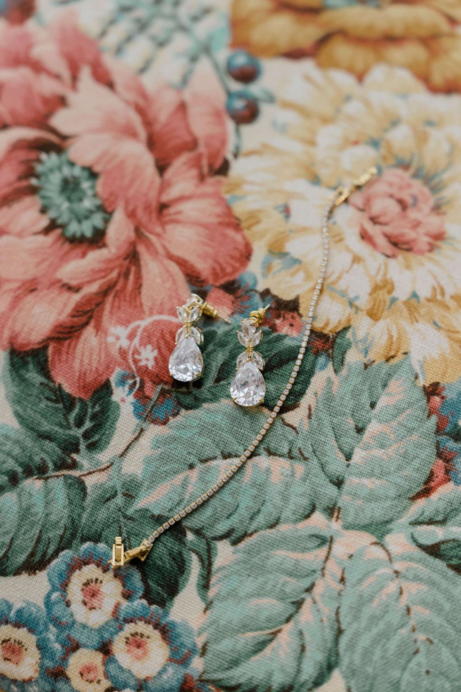 Crystal teardrop earrings and delicate gold bracelet displayed on vintage floral fabric.