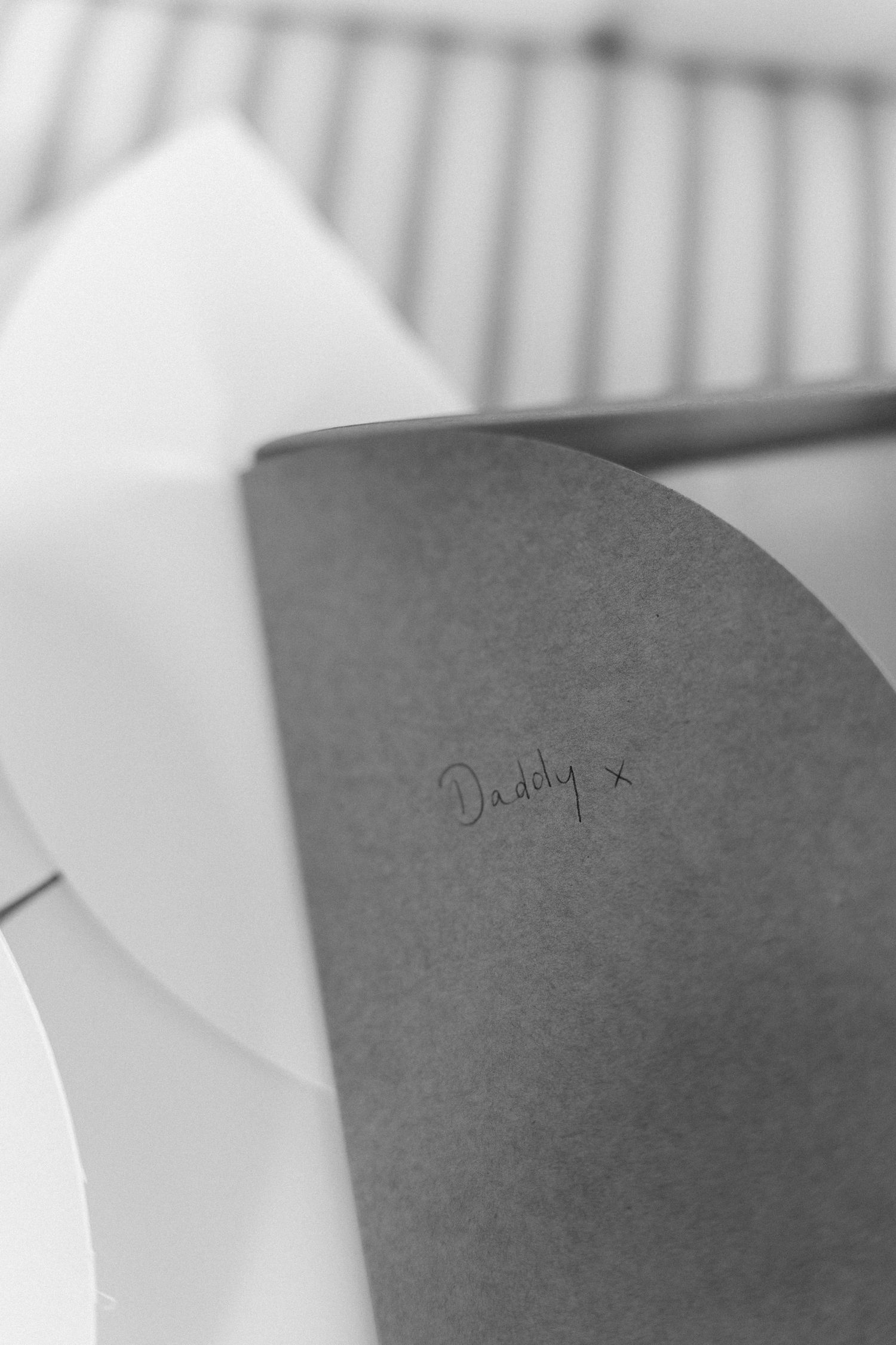 Black and white close-up of a grey envelope handwritten with Daddy x resting against a metal rack.