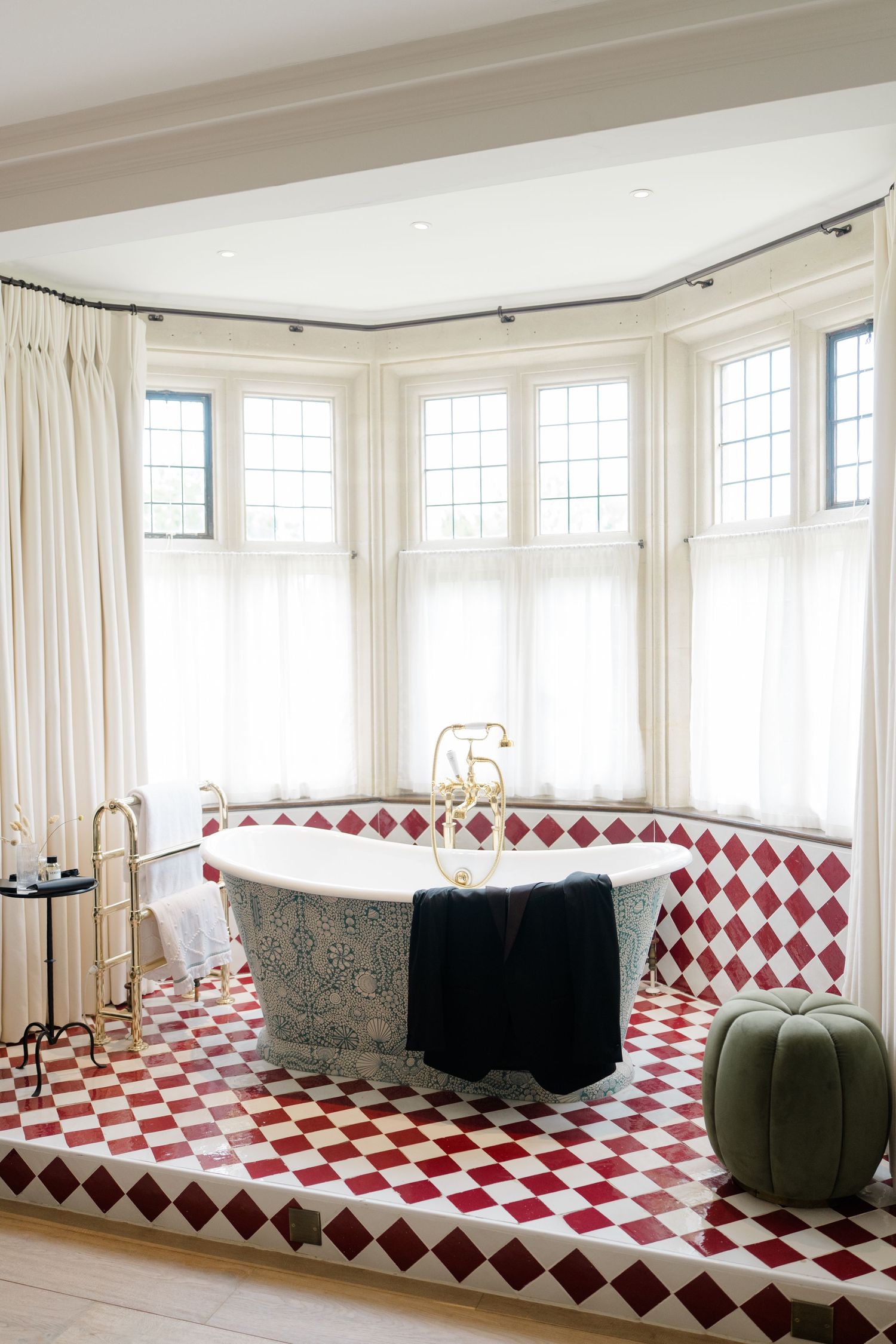 Luxurious freestanding bathtub on raised red diamond tile platform with bay windows in elegant bridal suite.
