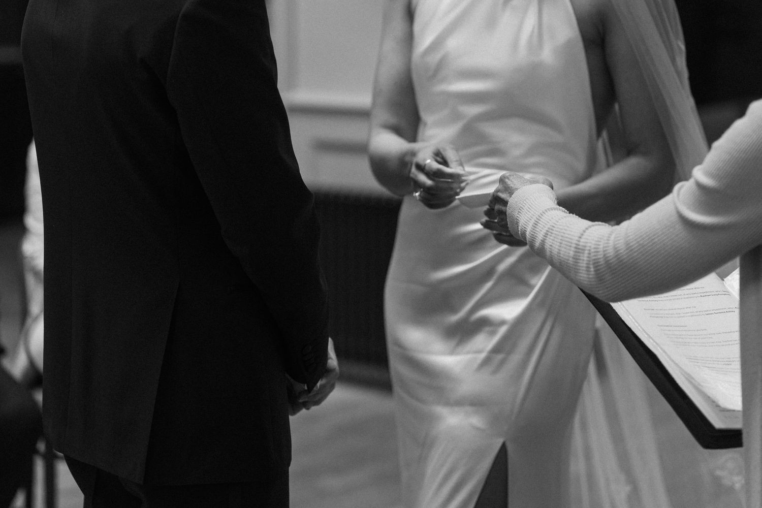 Close-up black and white photo of bride placing wedding ring on grooms hand during ceremony.