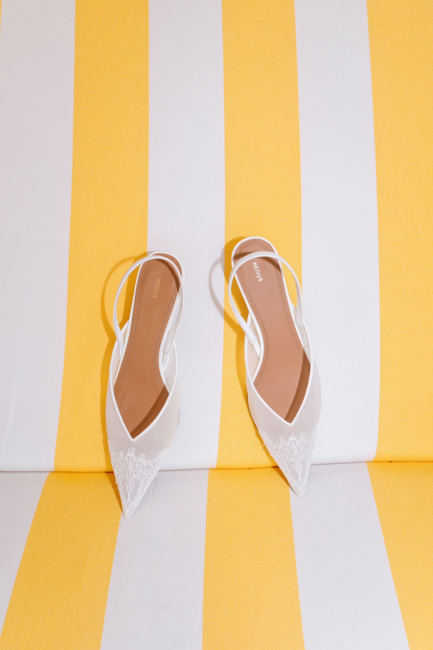 White lace slingback heels against yellow and white striped background.