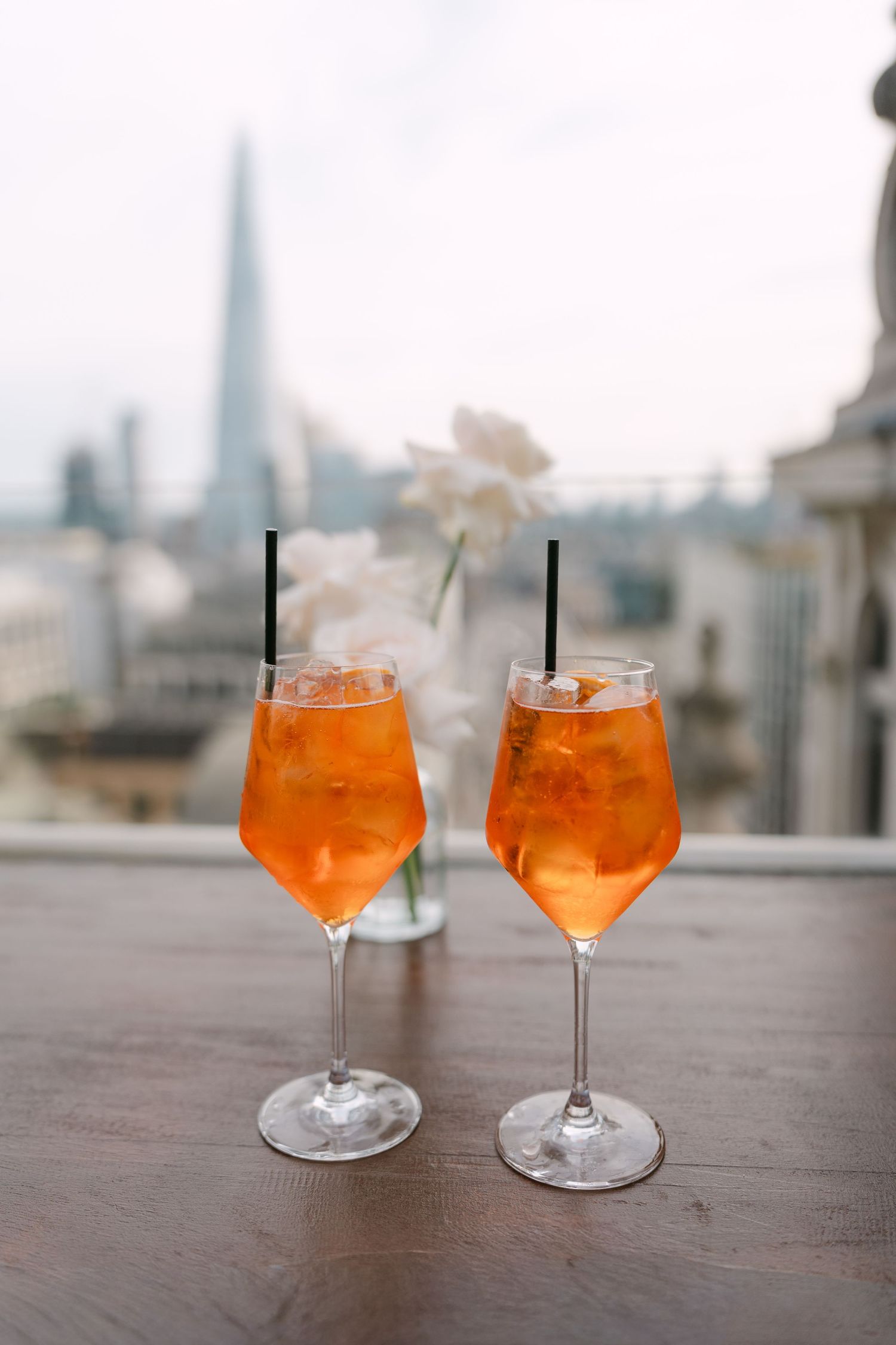 Two orange cocktails in wine glasses with a city skyline view in background.
