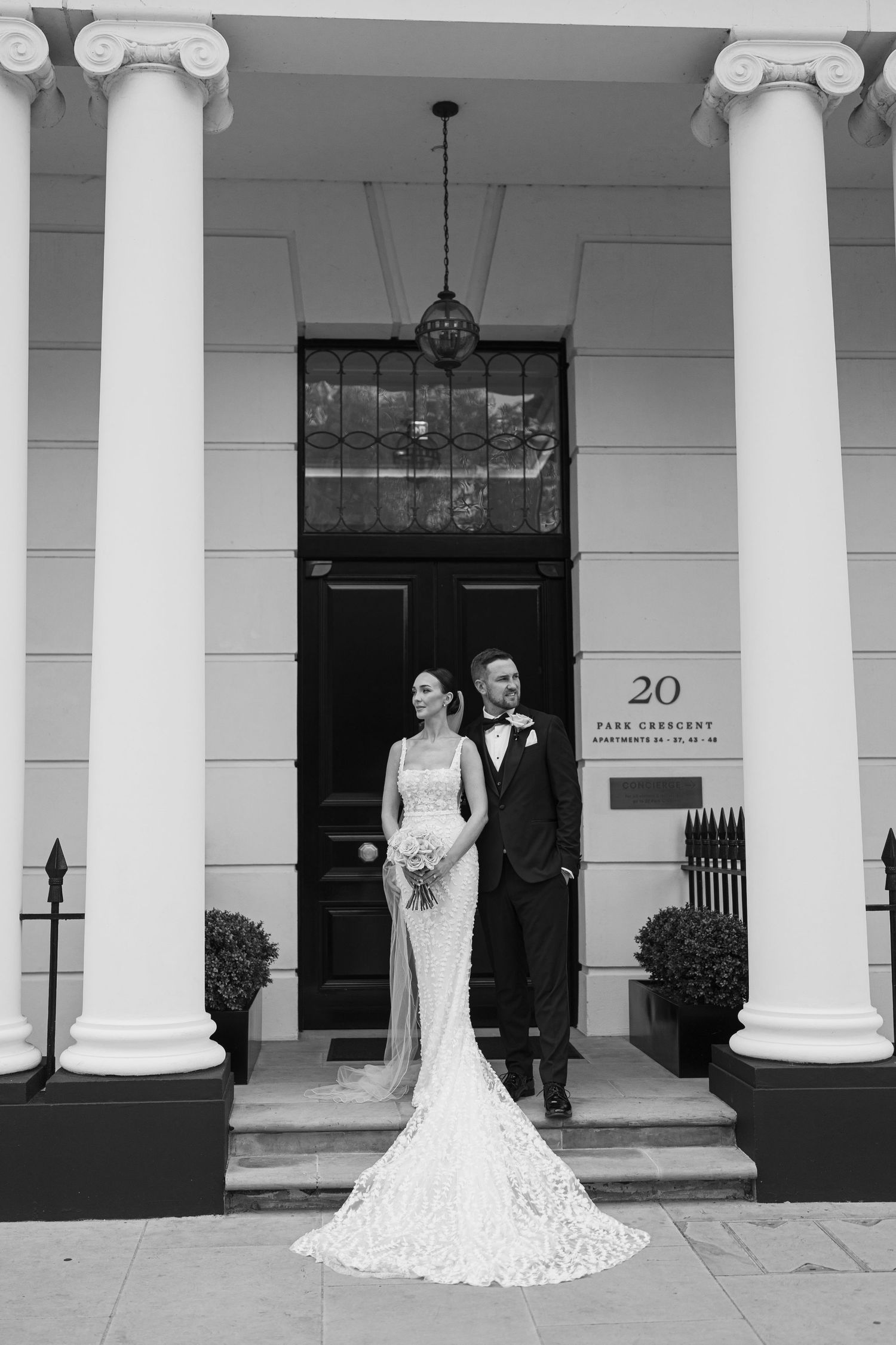 Classic wedding portrait of couple standing between white columns at elegant venue entrance.