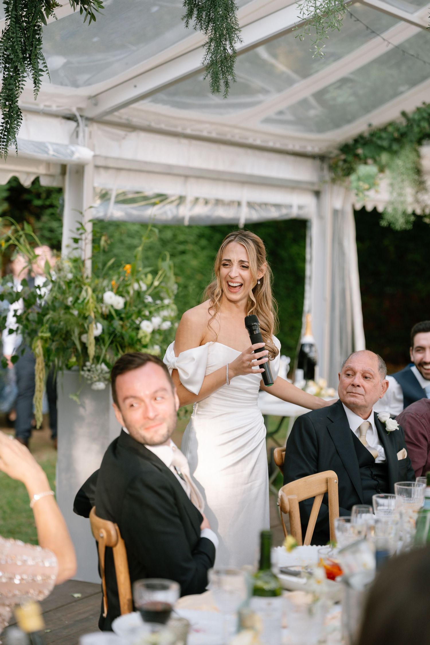 Wedding reception celebration in an outdoor tent with guests seated at decorated tables.