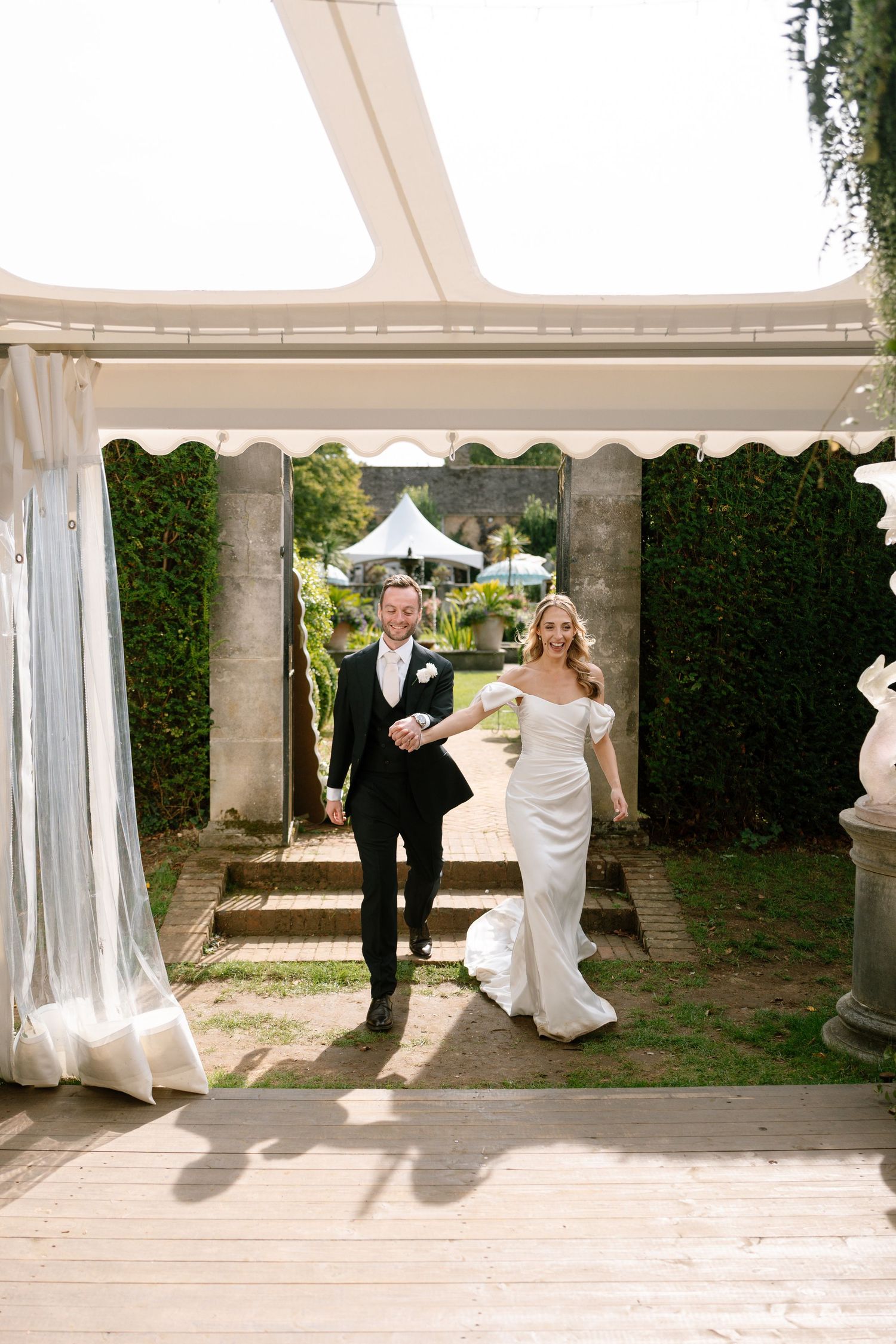 Newlyweds walking through elegant garden archway decorated with greenery.