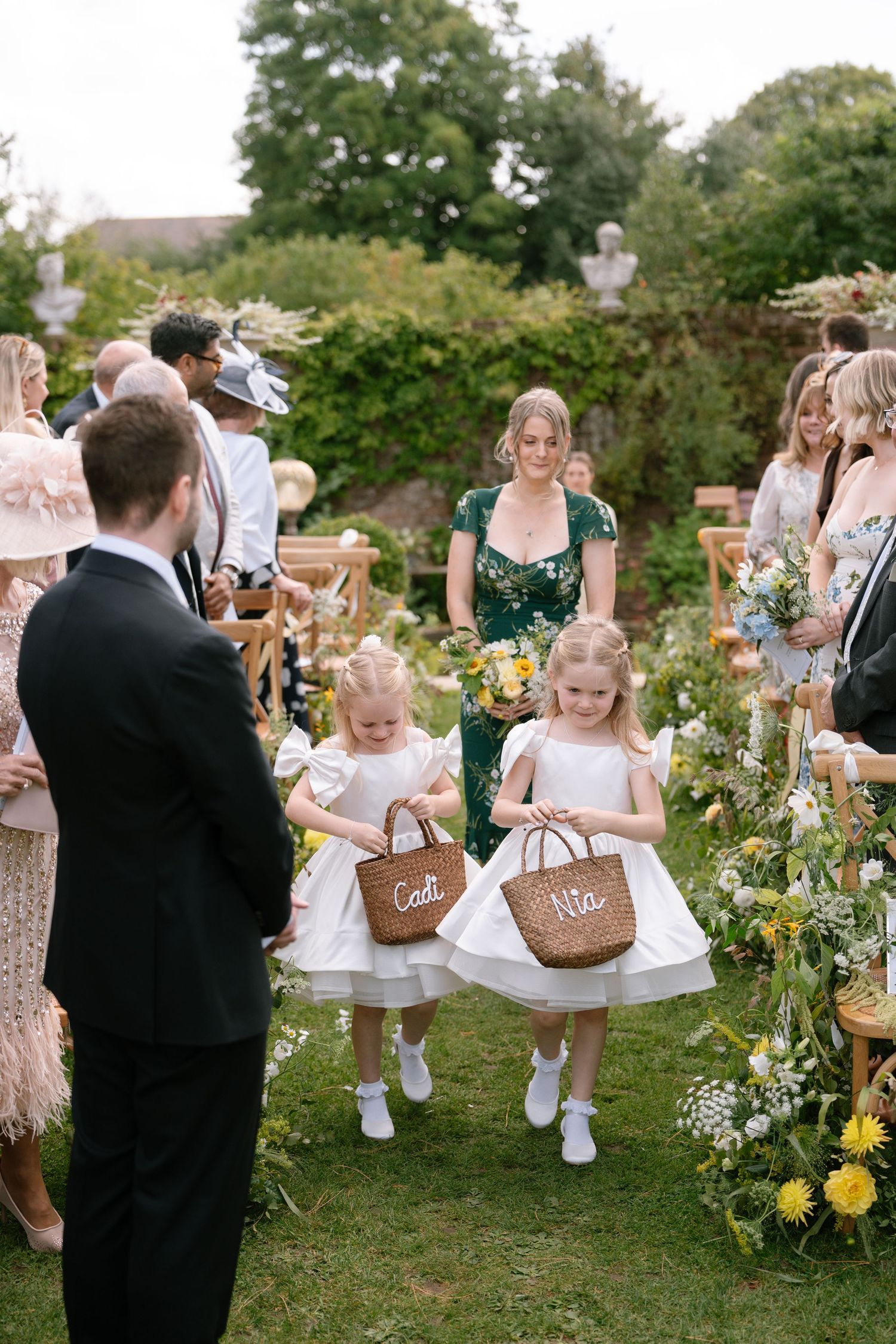 Wedding guests mingle outdoors among floral decorations and garden furniture.