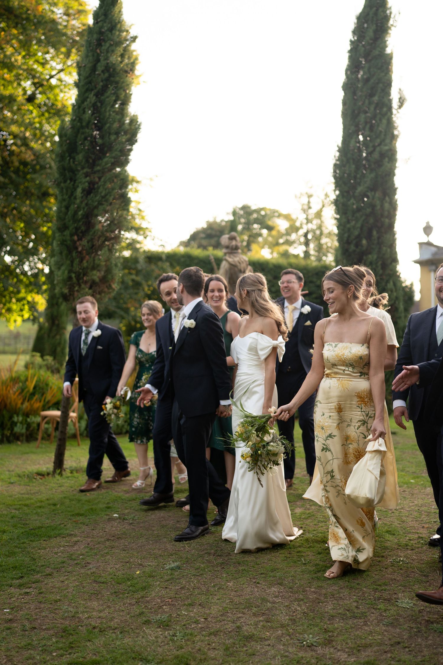 Wedding celebration outdoors with formal attire and gold dresses against late afternoon sunlight.