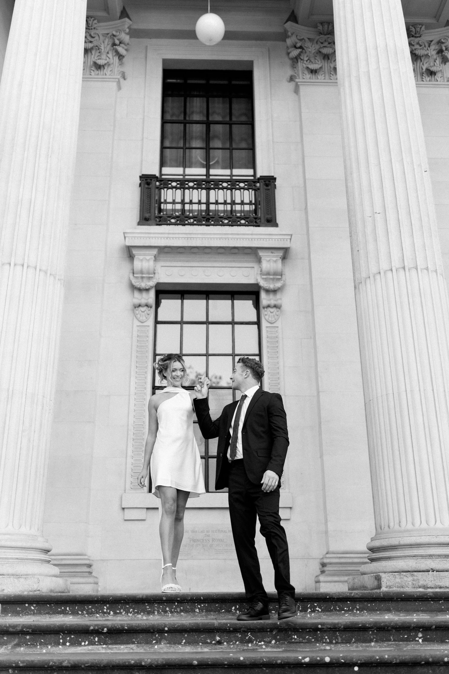 A couple shares an intimate moment between white columns of a classical building.