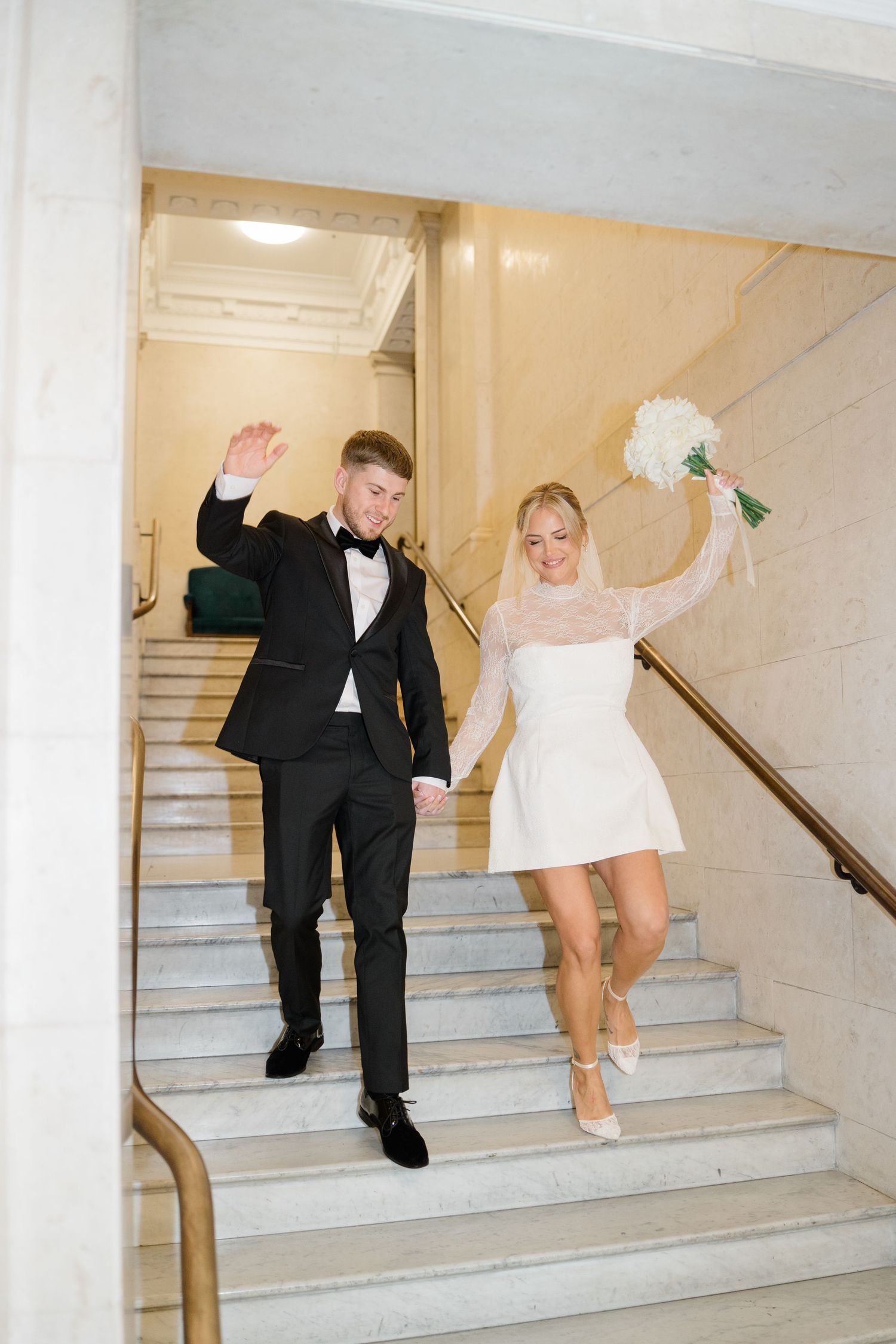 Playful sequence of a bride and groom walking up white marble stairs in formal wedding attire.