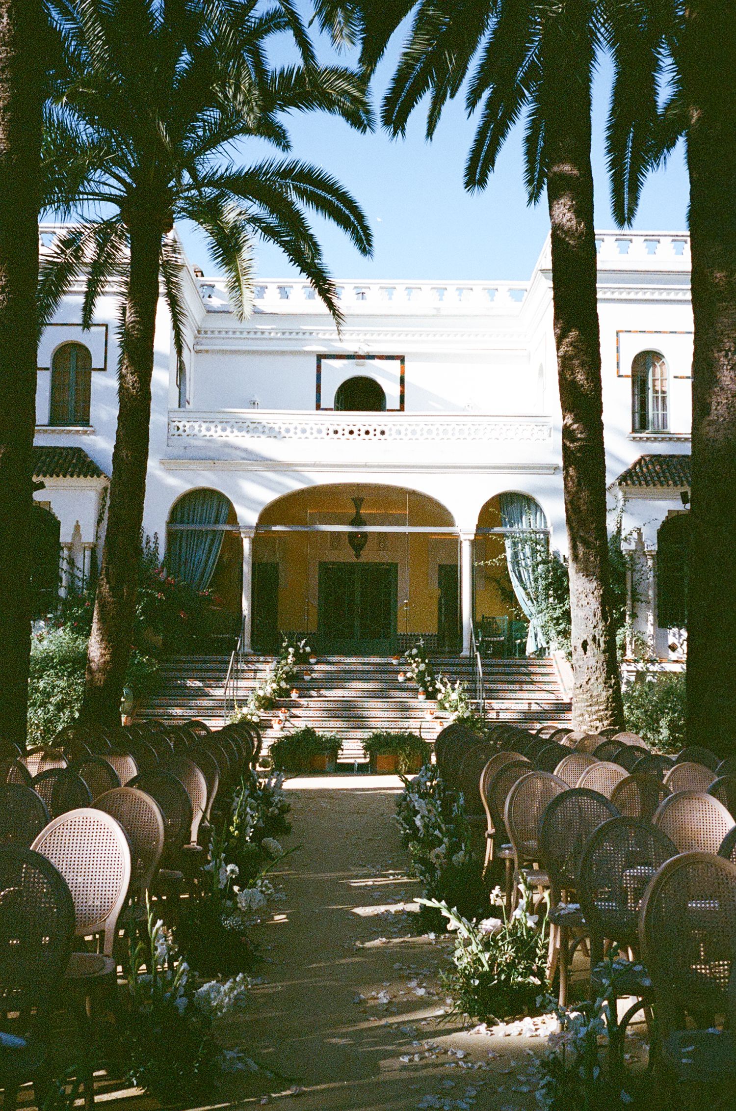 Elegant outdoor venue with white Mediterranean-style architecture and palm trees creating a shaded seating area.
