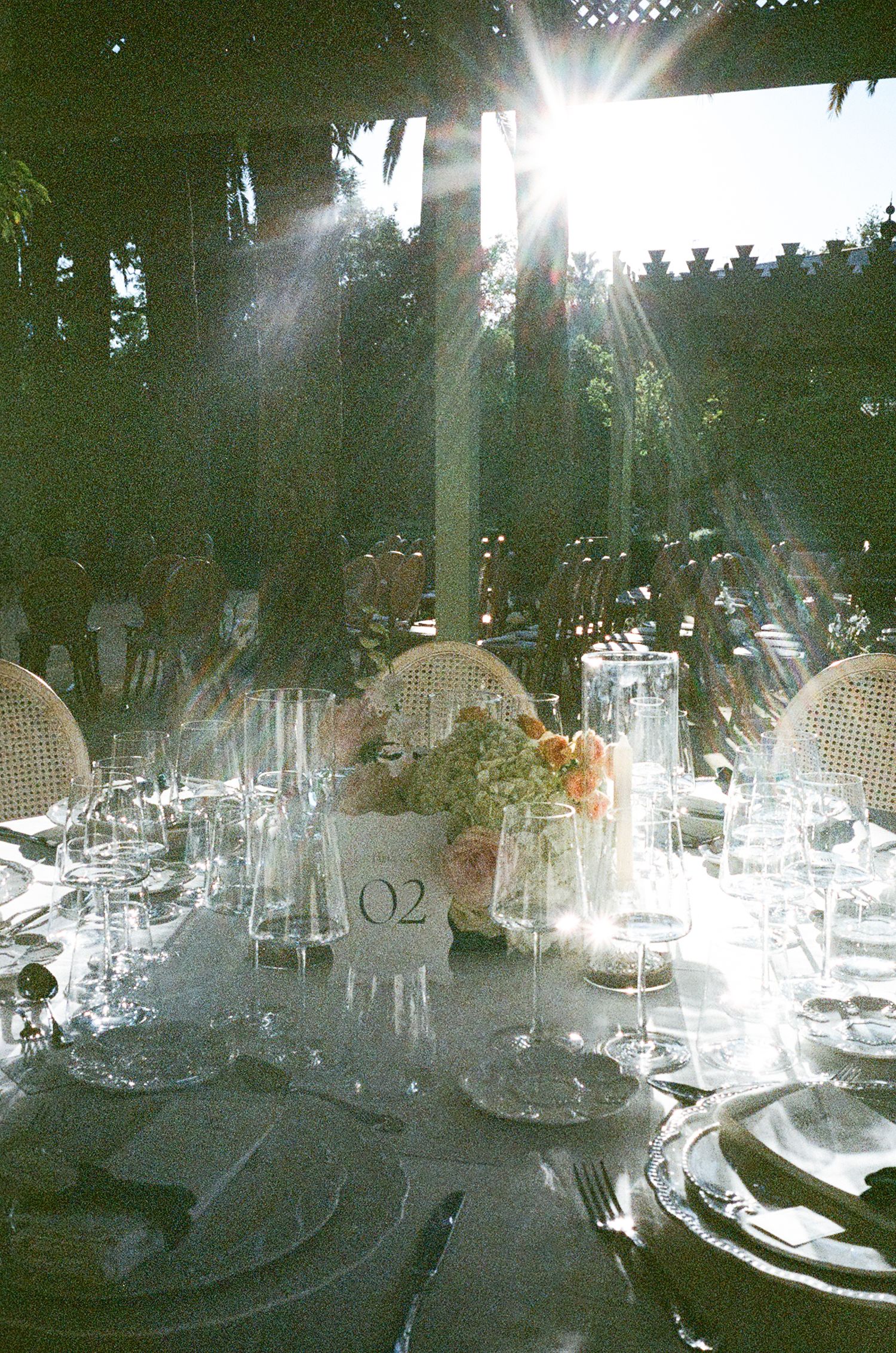 Multiple elegant table settings with glassware and decorative elements at an indoor event venue under soft lighting.
