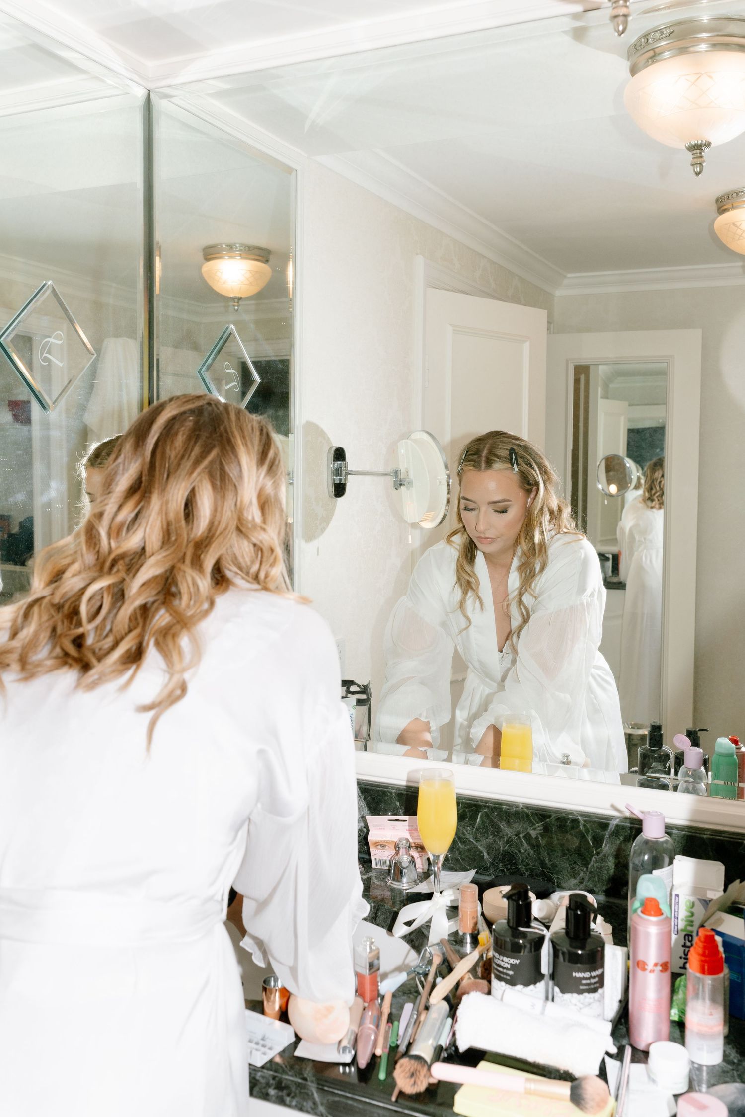 Bright makeup station with mirrors and beauty products arranged on white counter in professional styling space.