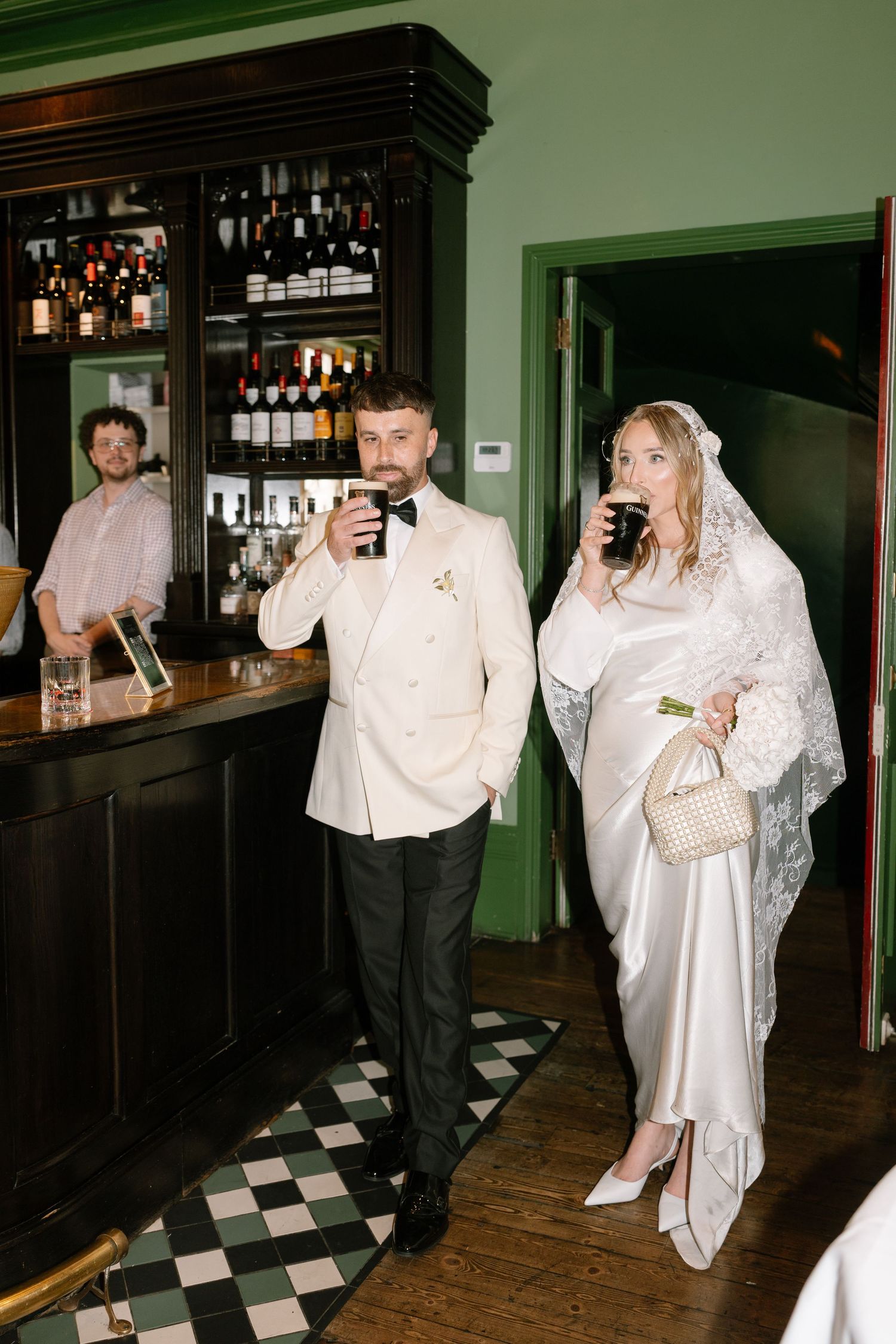 A couple enjoys drinks at a vintage bar with wooden shelves stocked with wine and spirits.