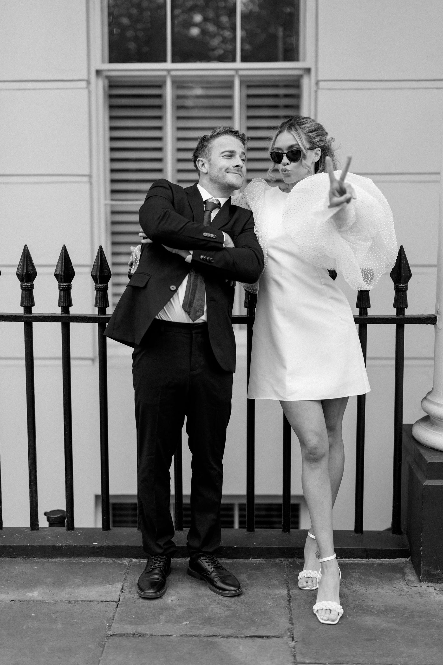 Black and white series of playful poses against an iron fence in an urban setting.