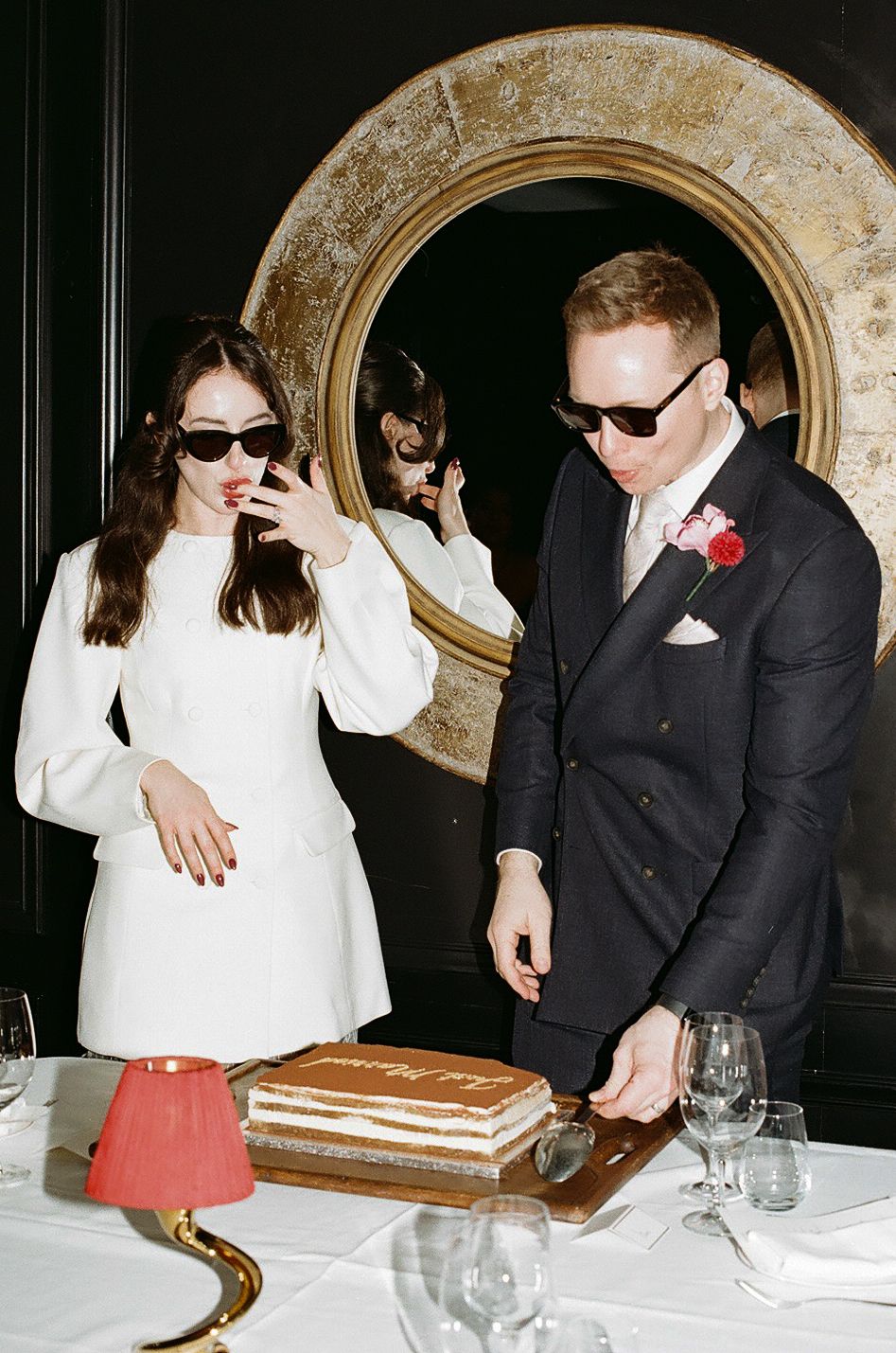 A couple in formal attire shares a playful moment at a restaurant table with white tablecloth and wine glasses.